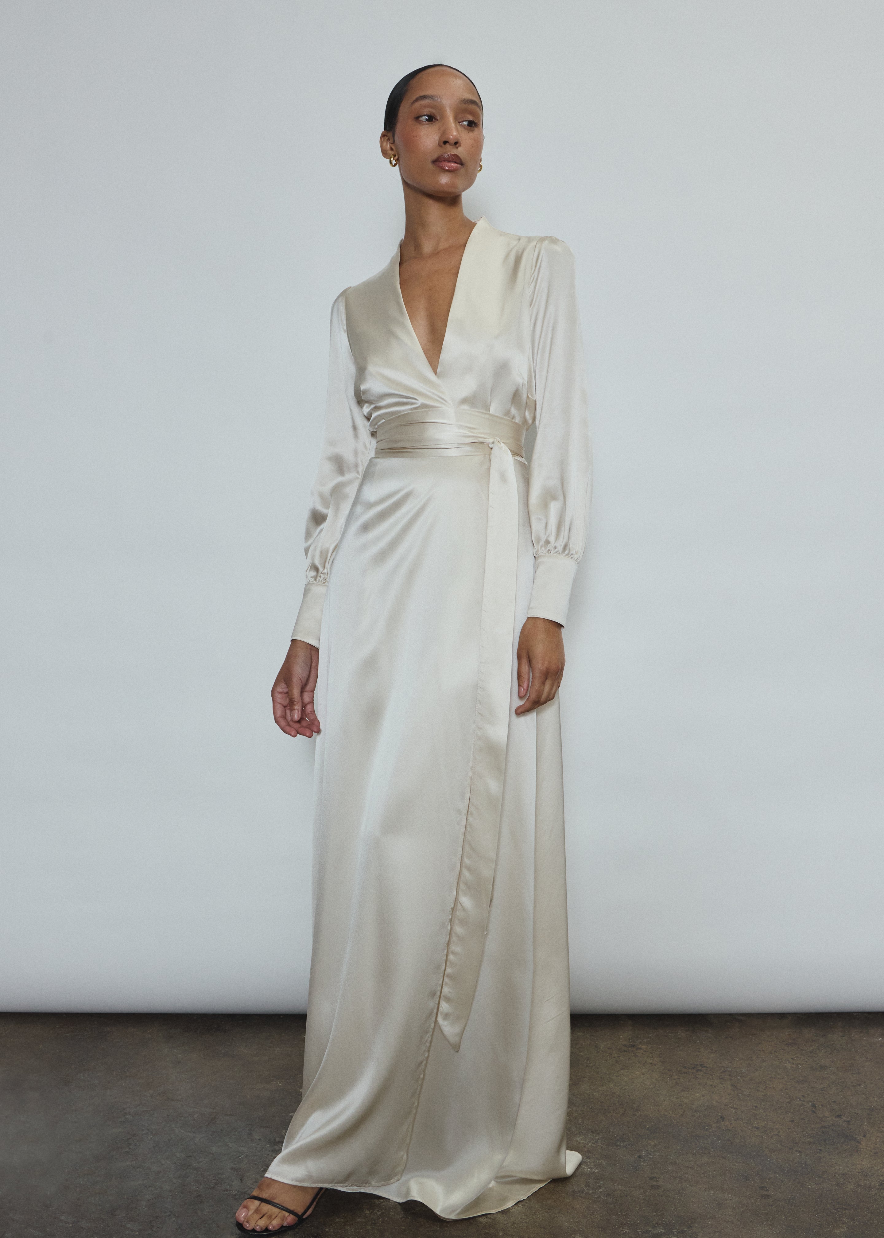 Full-length view of a bride wearing the ivory silk charmeuse Adelaide wrap gown, featuring voluminous sleeves with button cuffs and a plunging neckline.