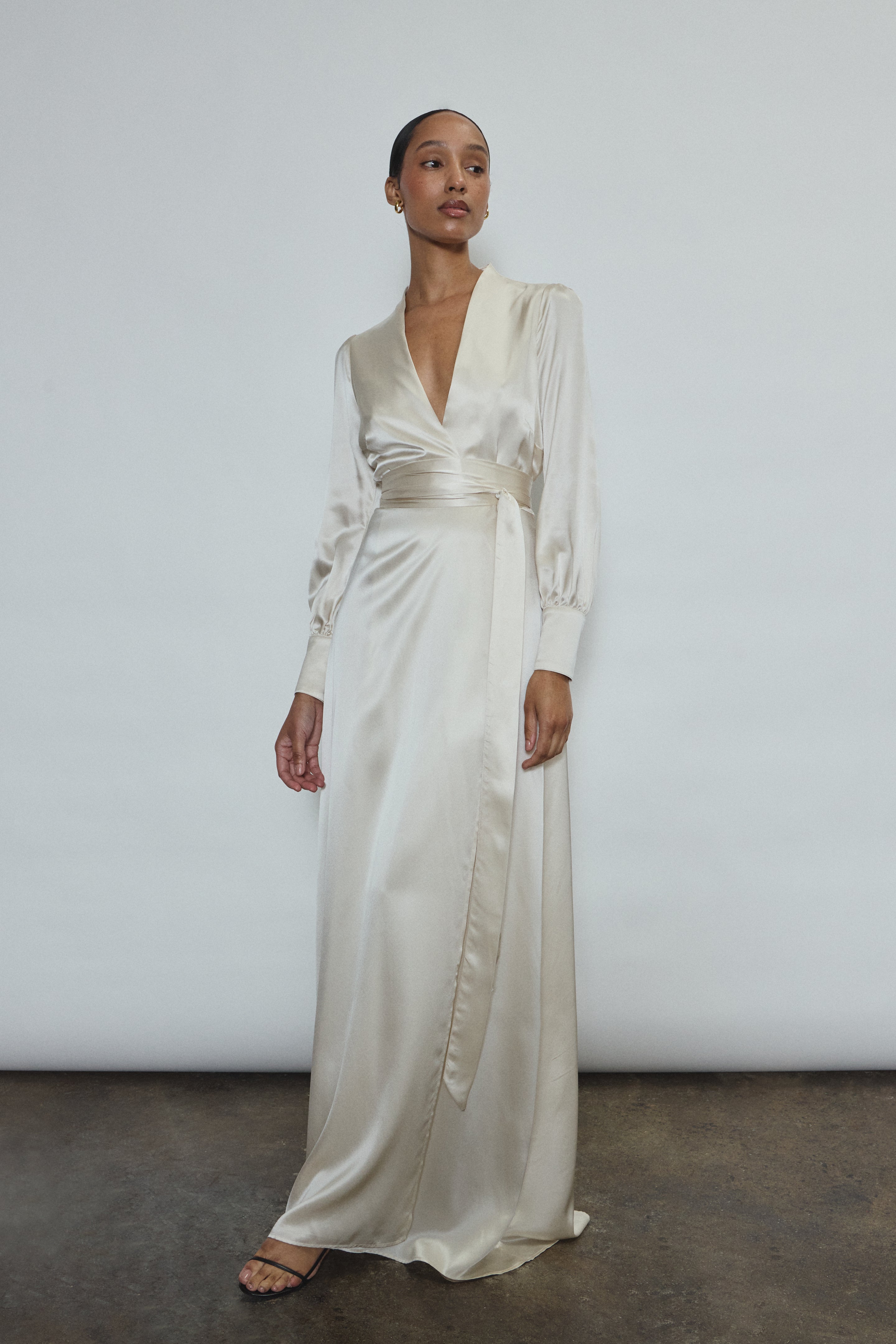 Full-length view of a bride wearing the ivory silk charmeuse Adelaide wrap gown, featuring voluminous sleeves with button cuffs and a plunging neckline.