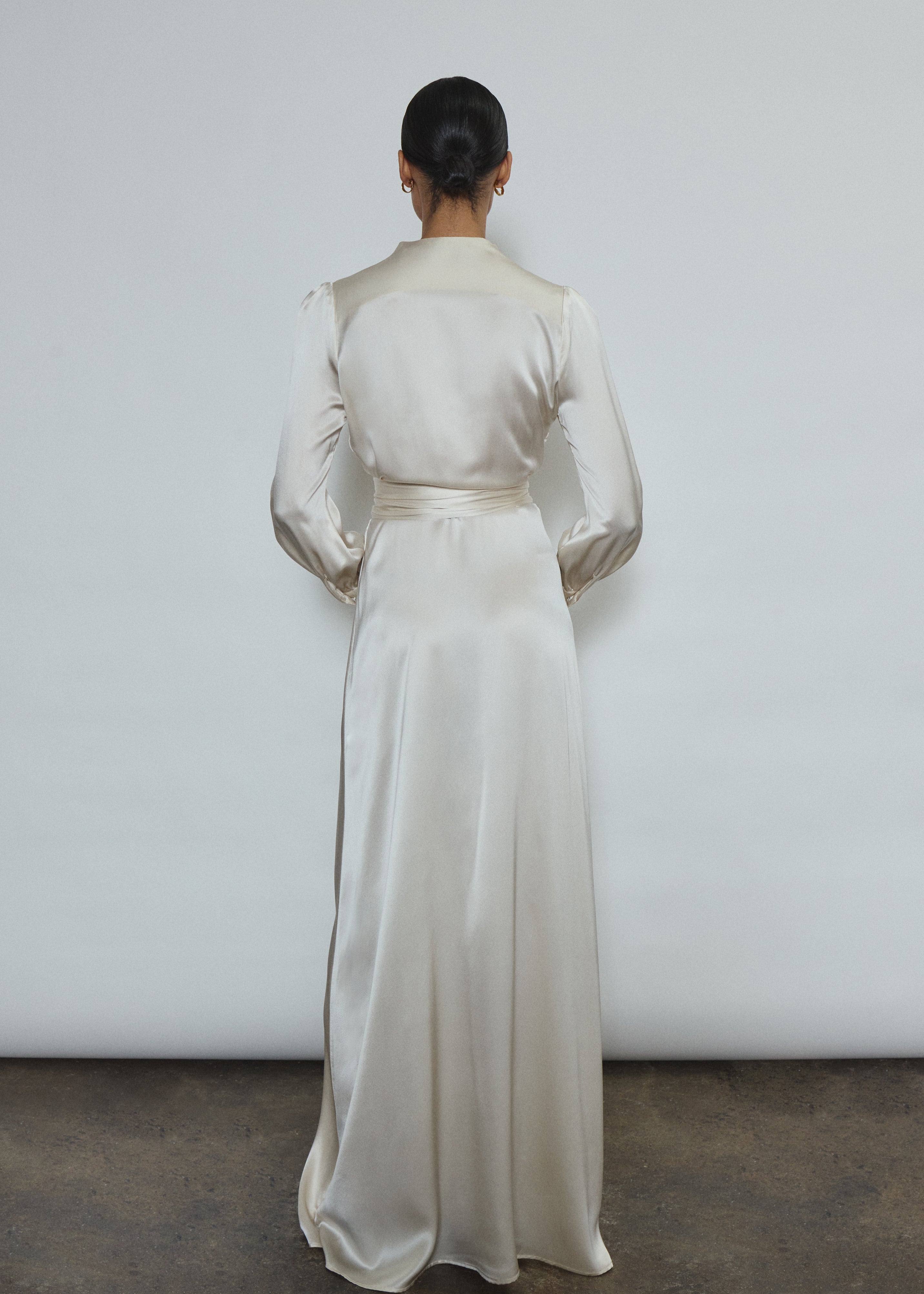 Full-length view of a bride wearing the ivory silk charmeuse Adelaide wrap gown, featuring voluminous sleeves with button cuffs and a plunging neckline.