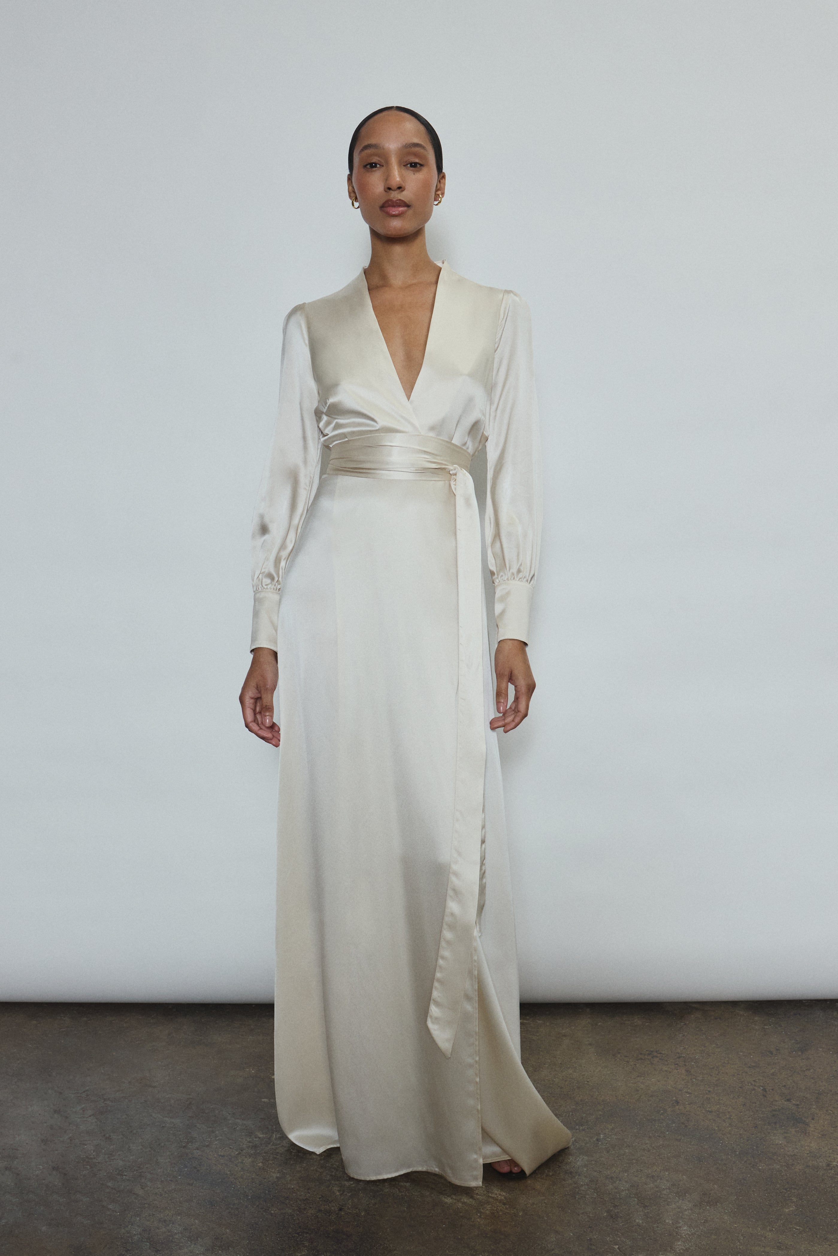 Full-length view of a bride wearing the ivory silk charmeuse Adelaide wrap gown, featuring voluminous sleeves with button cuffs and a plunging neckline.