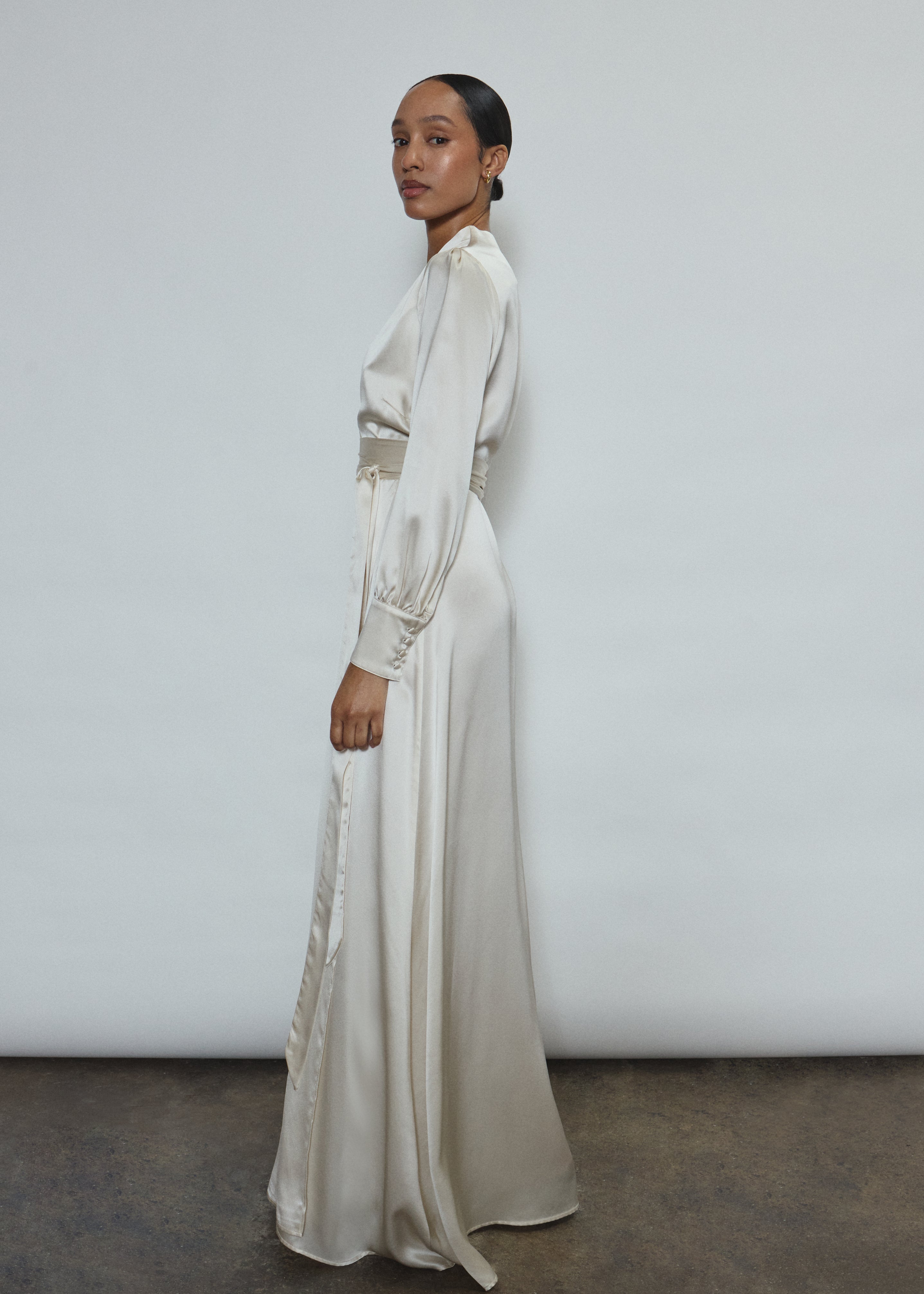 Full-length view of a bride wearing the ivory silk charmeuse Adelaide wrap gown, featuring voluminous sleeves with button cuffs and a plunging neckline.