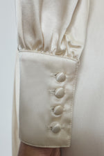 View of the sleeve detail of the ivory silk charmeuse Adelaide wrap gown with button details. 