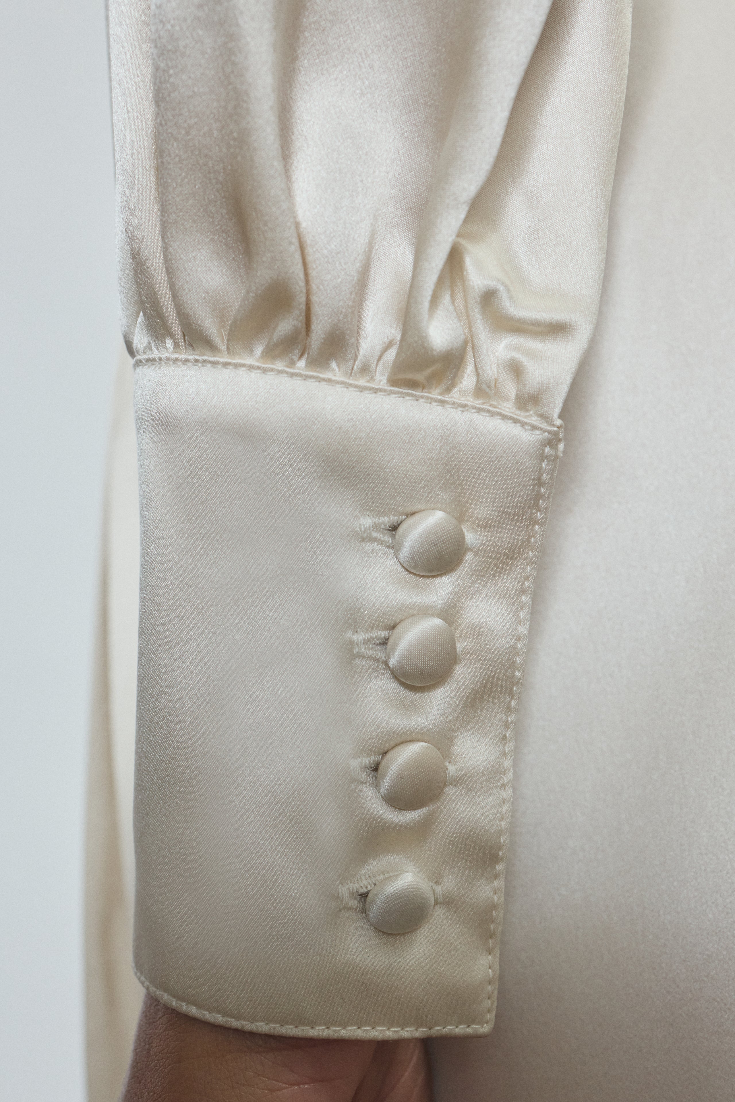 View of the sleeve detail of the ivory silk charmeuse Adelaide wrap gown with button details. 