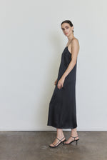 Side view of the black silk charmeuse Kamperett Agnes Slip Dress showing the loose midi silhouette and side pockets.