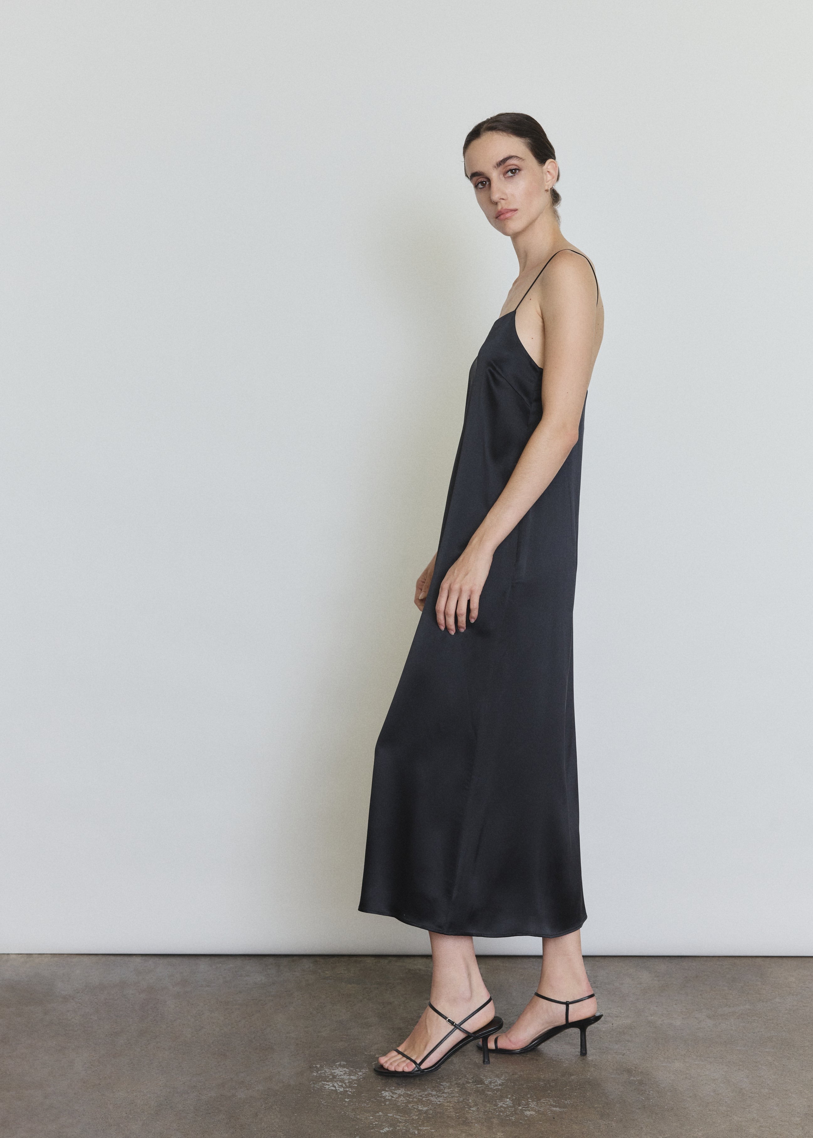 Side view of the black silk charmeuse Kamperett Agnes Slip Dress showing the loose midi silhouette and side pockets.