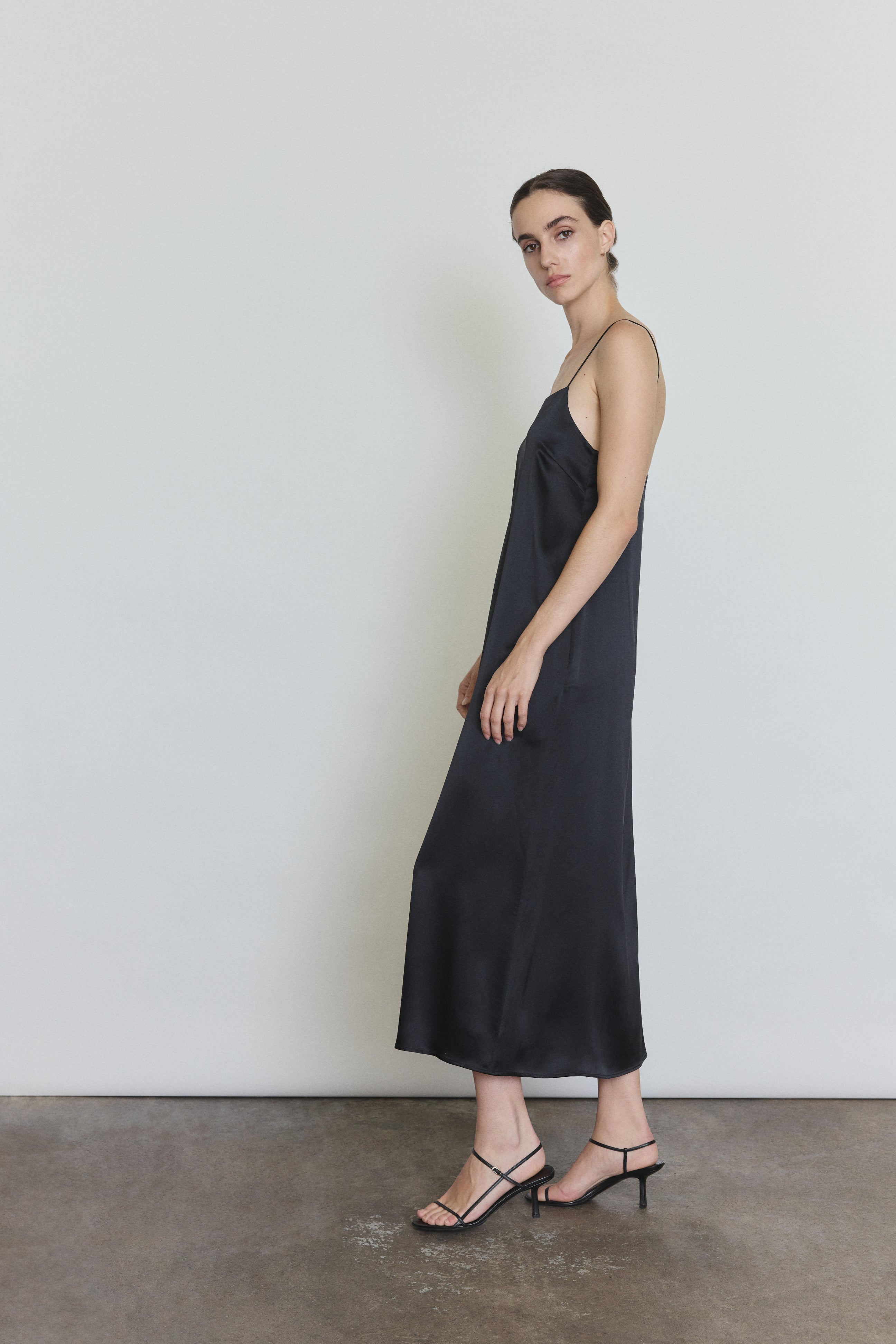 Side view of the black silk charmeuse Kamperett Agnes Slip Dress showing the loose midi silhouette and side pockets.