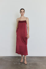 Front view of a model wearing the bordeaux silk charmeuse Kamperett Agnes Slip Dress, a boxy midi slip with straight neckline and corded straps.
