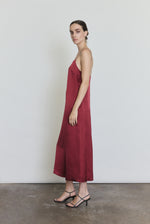 Side view of the bordeaux silk charmeuse Kamperett Agnes Slip Dress showing the loose midi silhouette and side pockets.