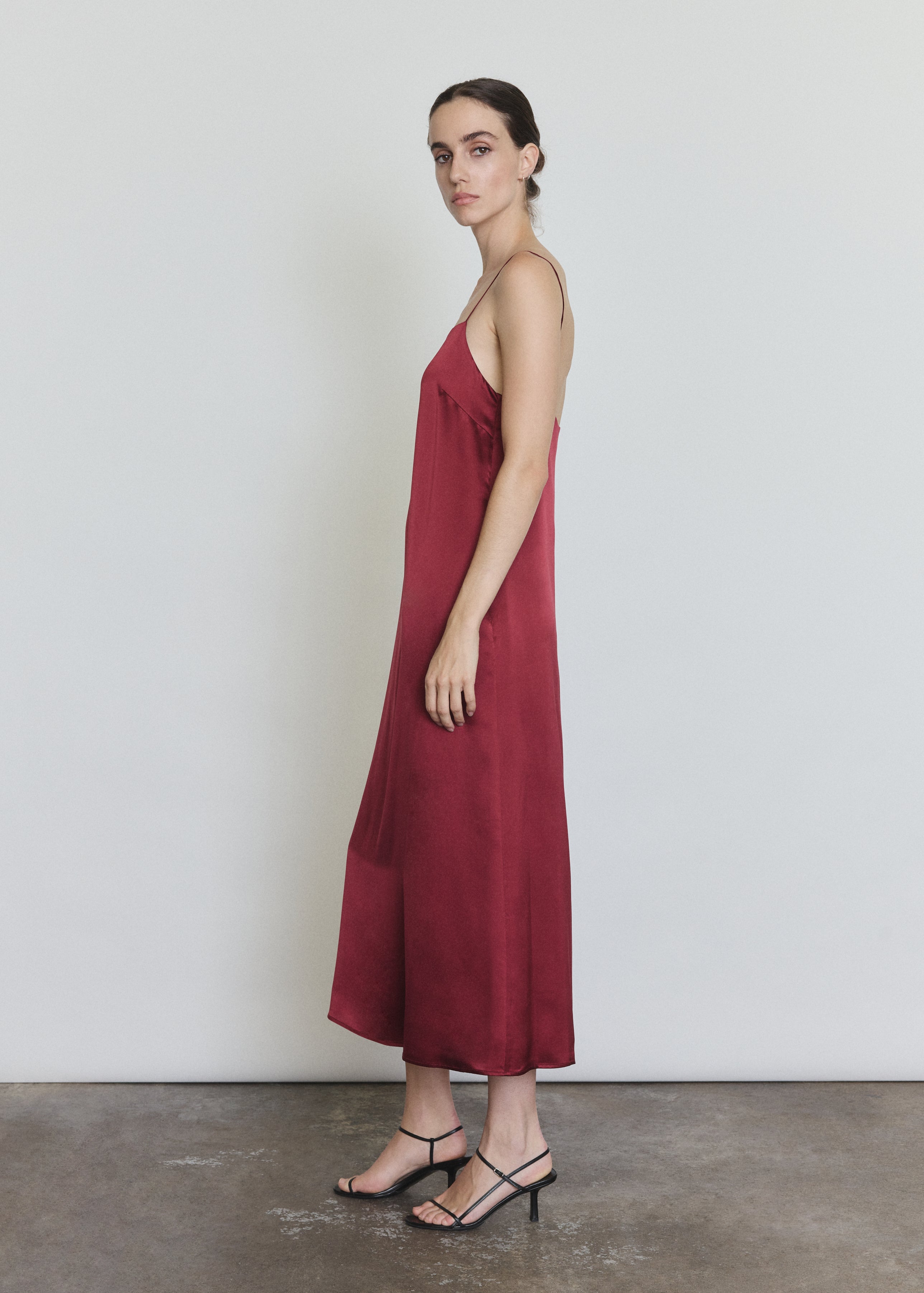 Side view of the bordeaux silk charmeuse Kamperett Agnes Slip Dress showing the loose midi silhouette and side pockets.