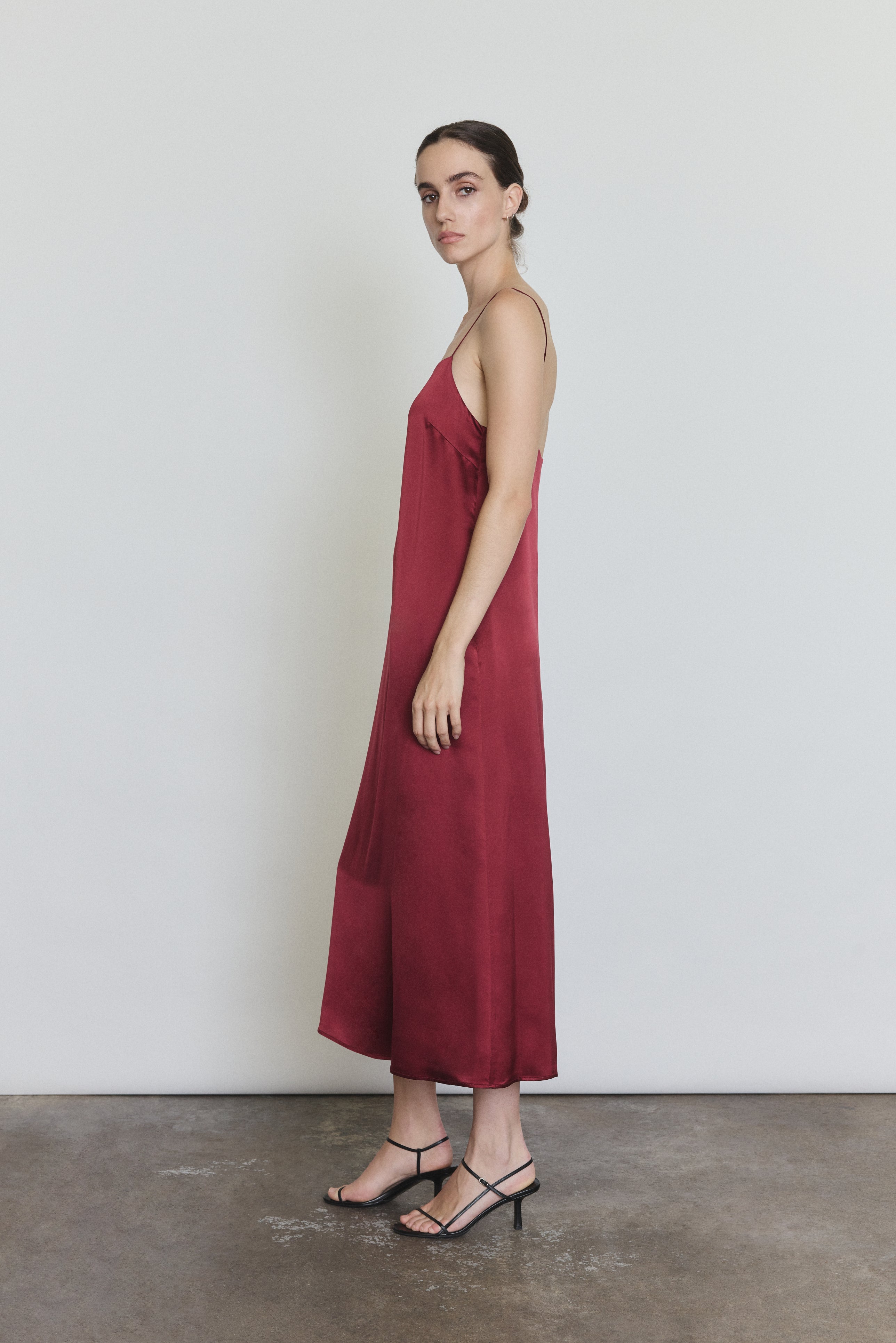 Side view of the bordeaux silk charmeuse Kamperett Agnes Slip Dress showing the loose midi silhouette and side pockets.