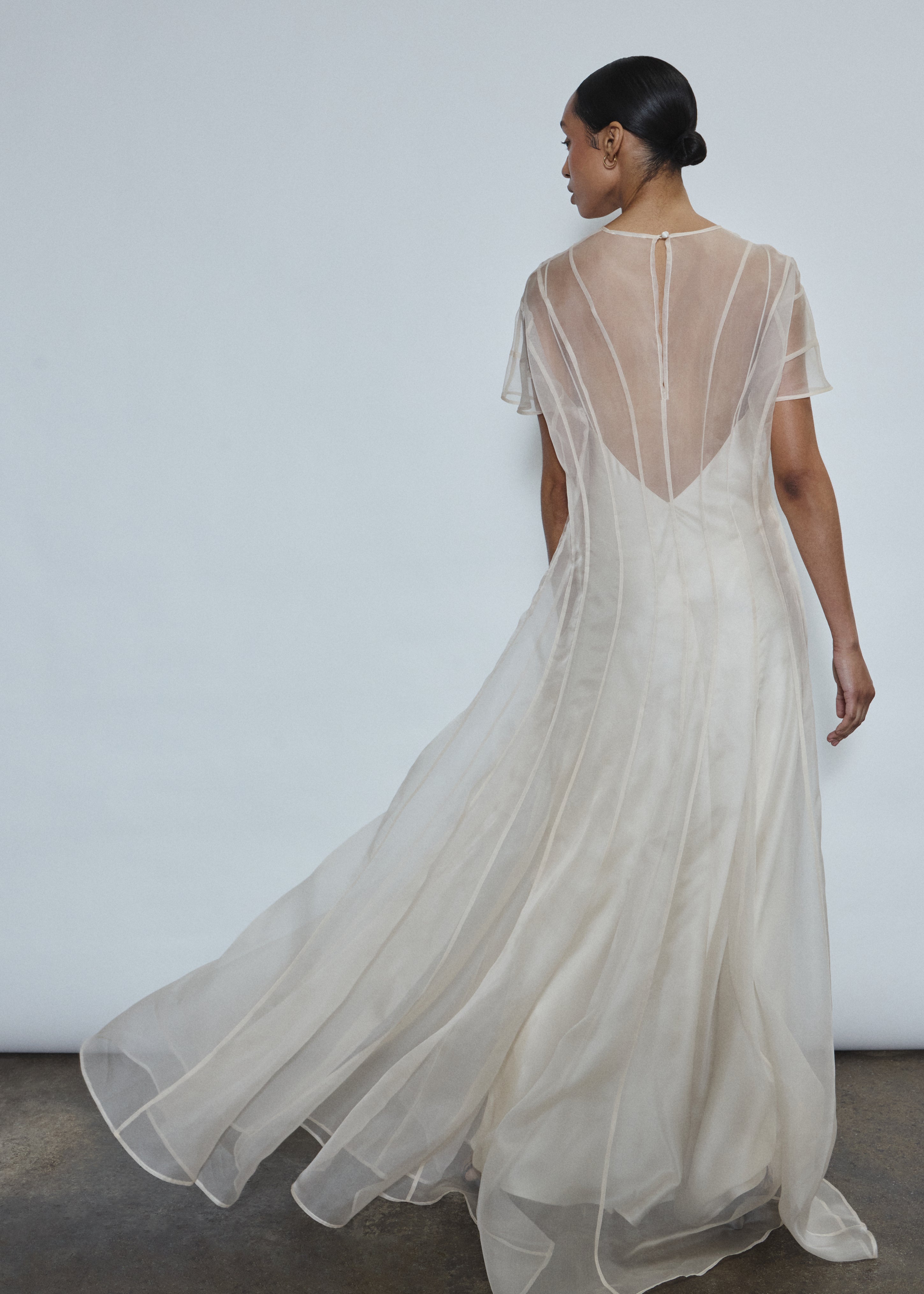 Rear view of ivory Anemoia Gown showing black silk button closure at center back neck. Architectural straight-cut silhouette in French lace organza.