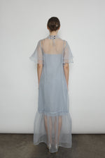 Model in a voluminous blue silk organza Barre maxi dress with oversized ruffles and tiered sleeves.