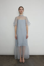 Model in a voluminous blue silk organza Barre maxi dress with oversized ruffles and tiered sleeves.