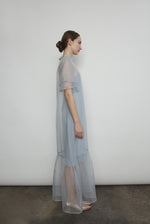 Model in a voluminous blue silk organza Barre maxi dress with oversized ruffles and tiered sleeves.