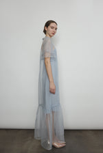 Model in a voluminous blue silk organza Barre maxi dress with oversized ruffles and tiered sleeves.