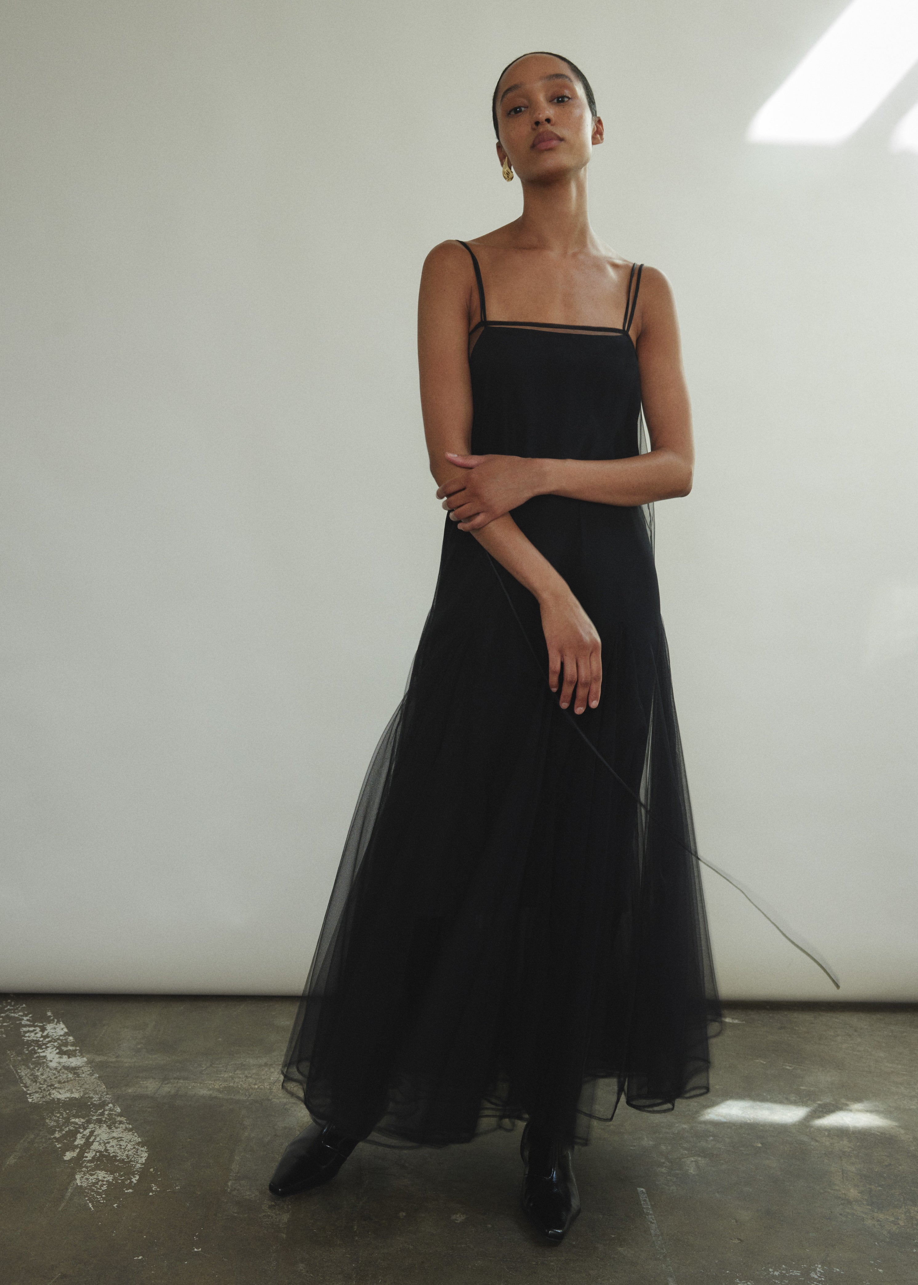 Model wearing the brown Kamperett Camille Dress, a sheer tulle tea-length overlay featuring adjustable silk corded straps and a voluminous godet-pleated skirt.