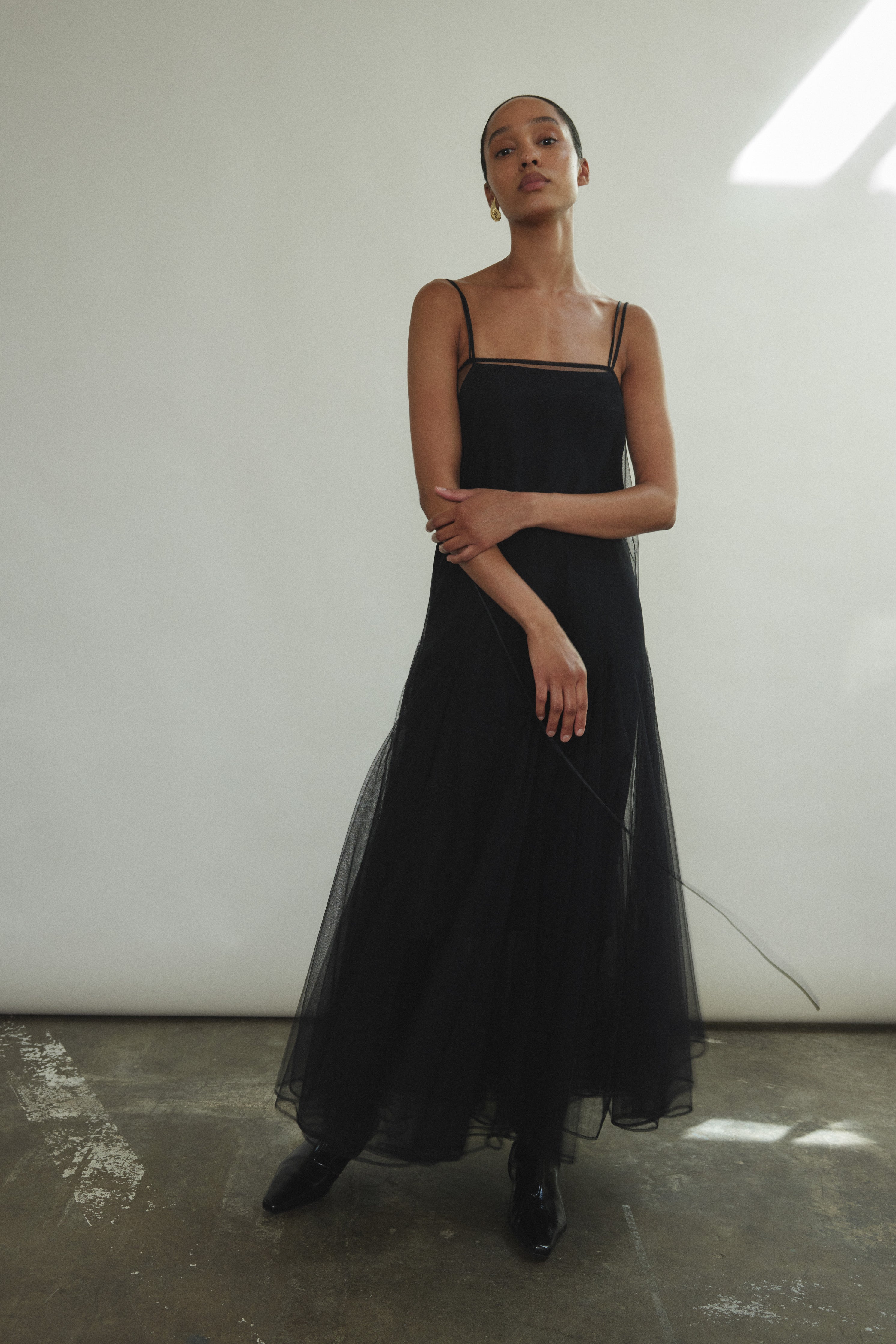 Front view of a model wearing the black sheer tulle Kamperett Camille Dress, a tea-length overlay with multi-godet skirt.