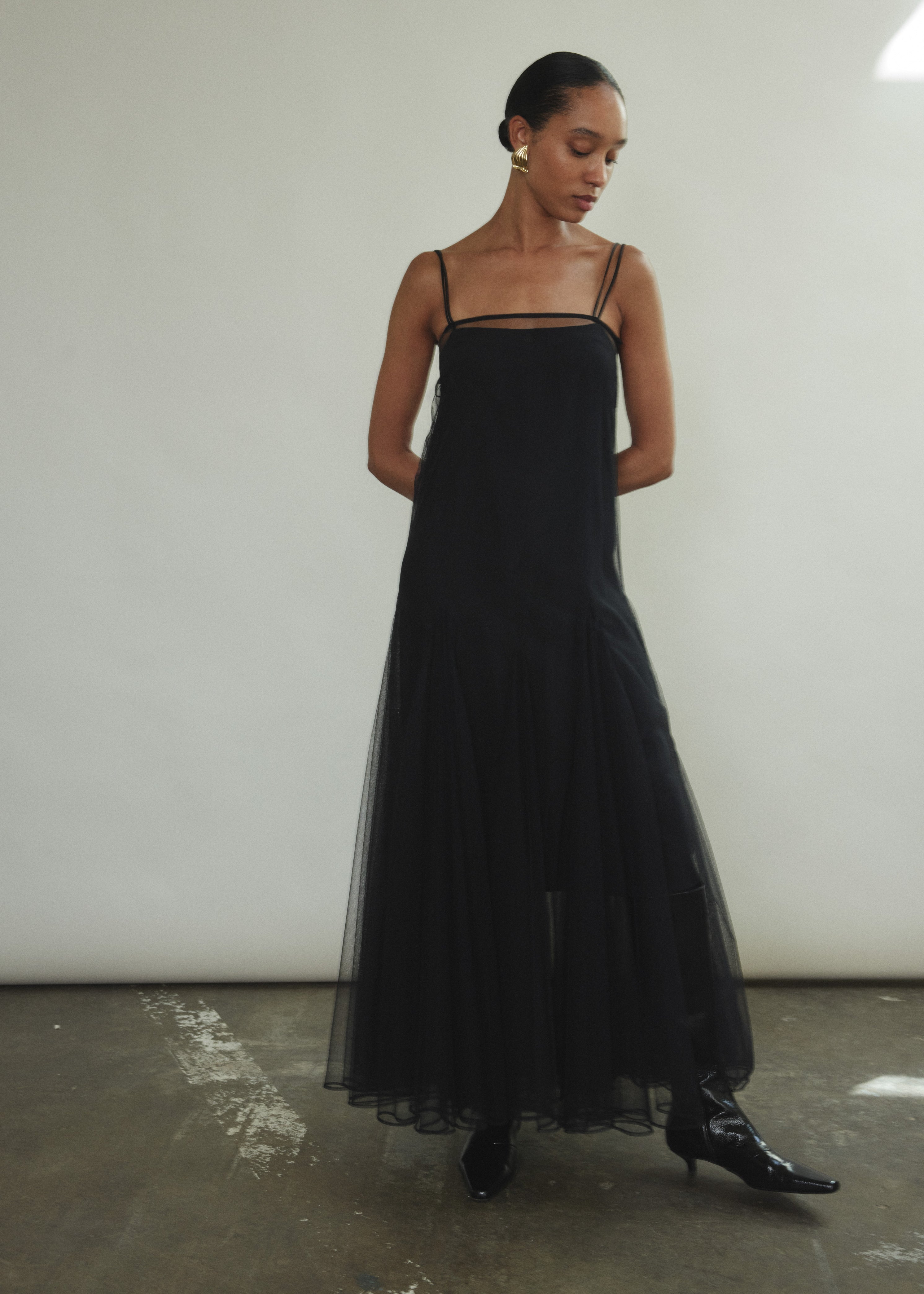 Model wearing the brown Kamperett Camille Dress, a sheer tulle tea-length overlay featuring adjustable silk corded straps and a voluminous godet-pleated skirt.