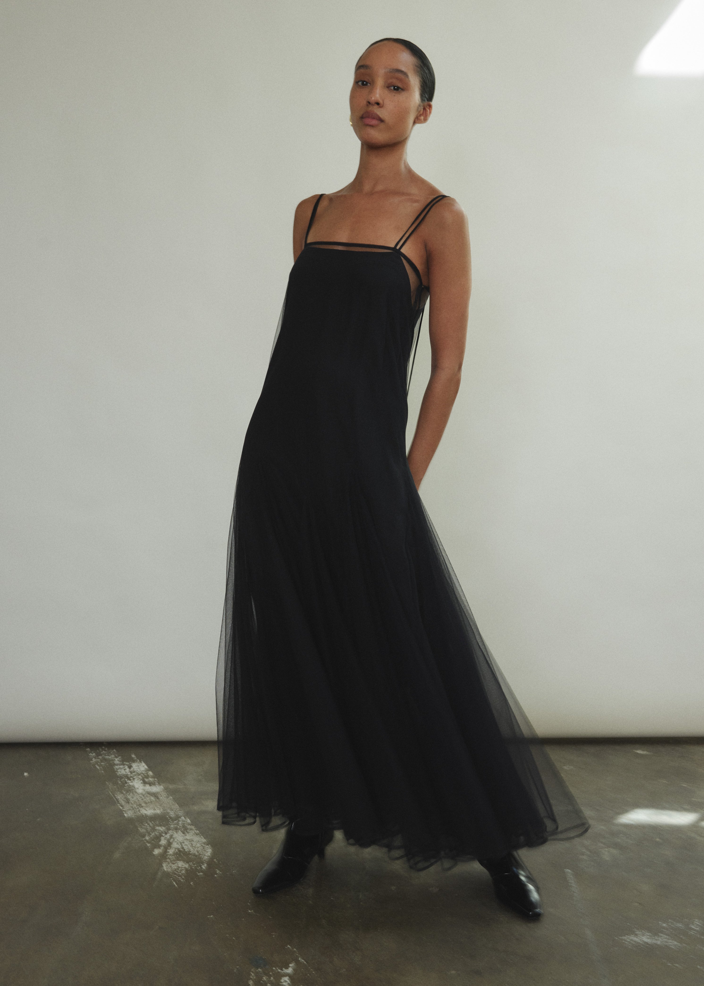 Model wearing the brown Kamperett Camille Dress, a sheer tulle tea-length overlay featuring adjustable silk corded straps and a voluminous godet-pleated skirt.