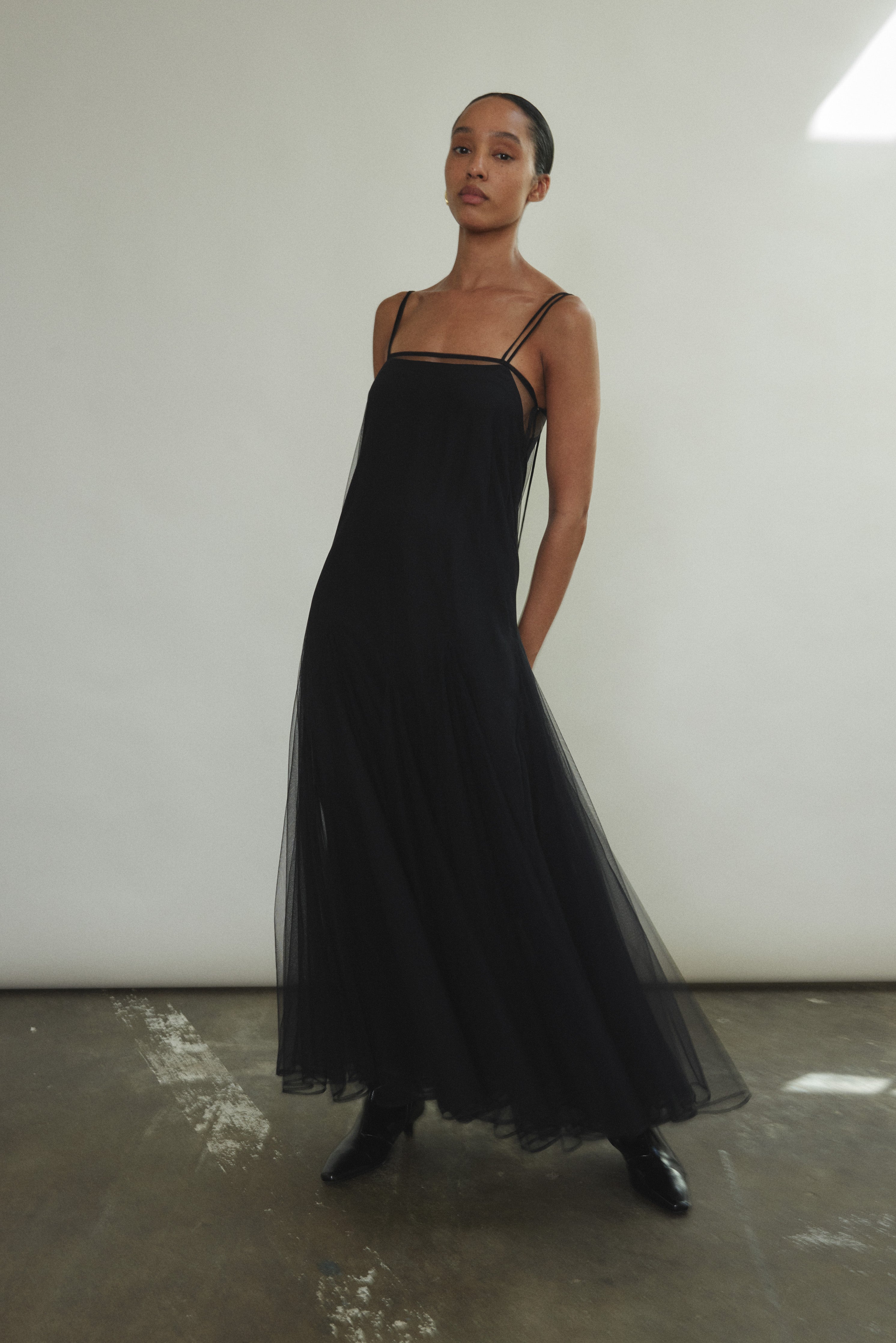 Motion shot of the black sheer tulle Kamperett Camille Dress, capturing the movement of the godet-pleated skirt.