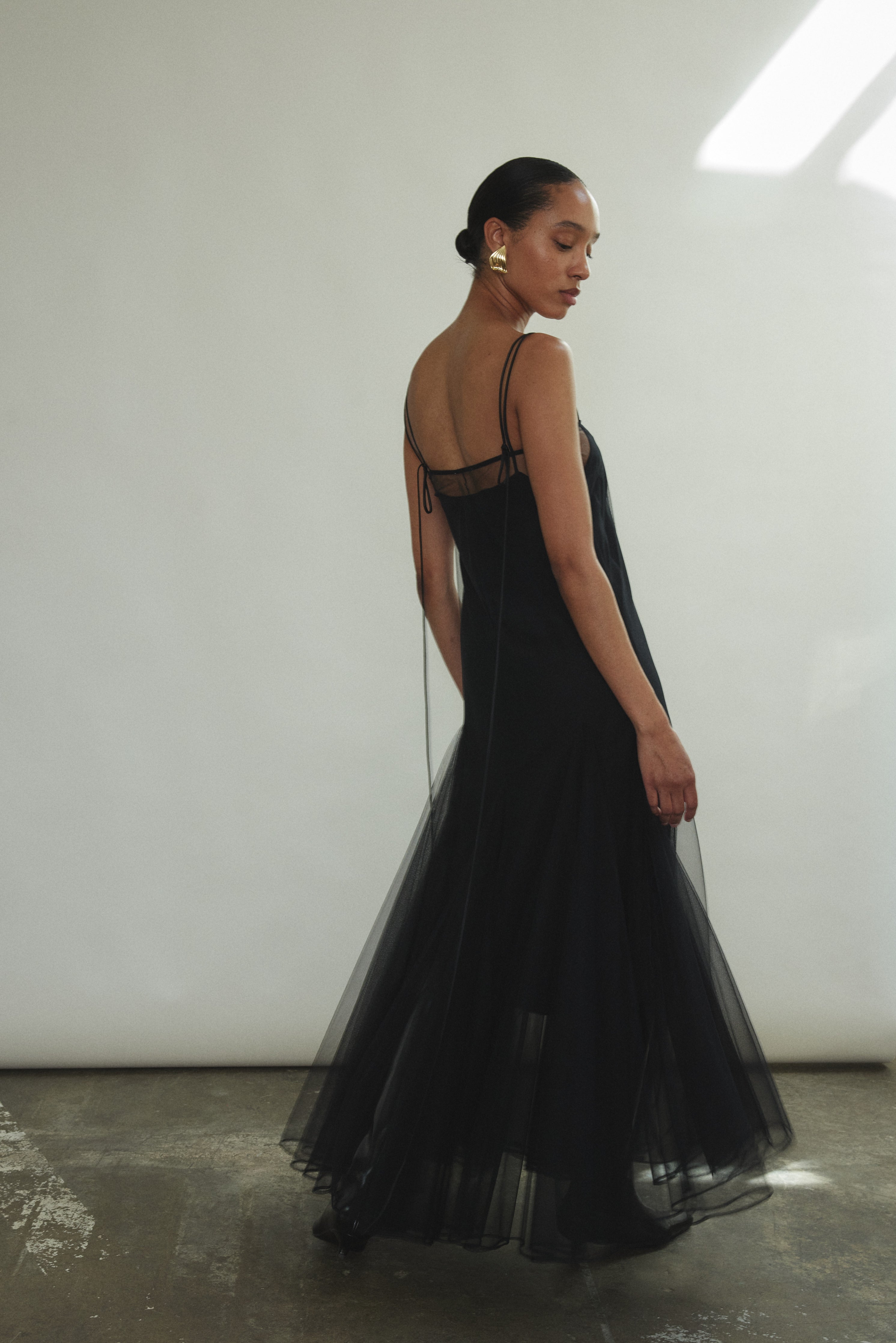 Side angle view of the black sheer tulle Kamperett Camille Dress, showing the godet skirt opening into fullness.