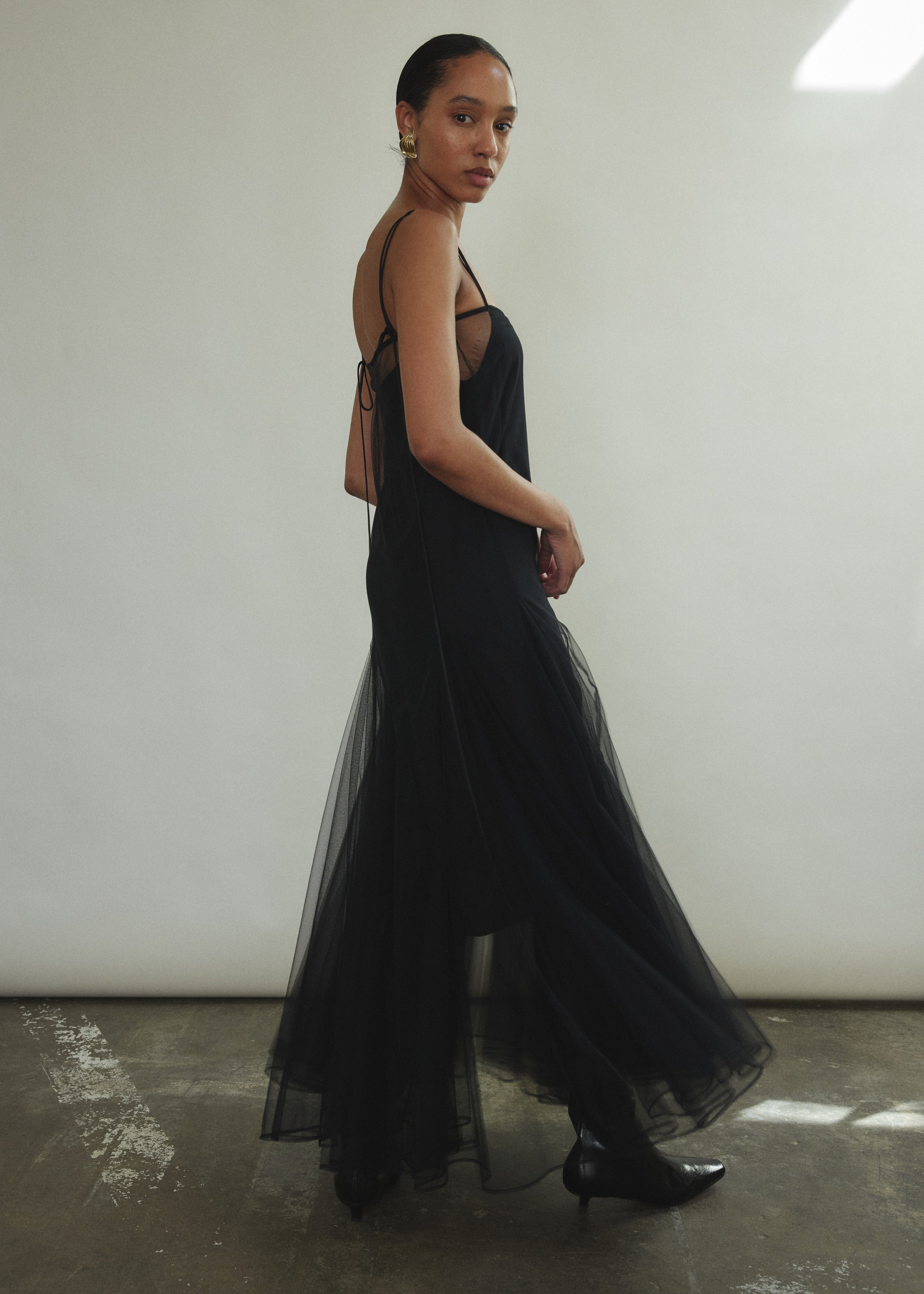 Model wearing the brown Kamperett Camille Dress, a sheer tulle tea-length overlay featuring adjustable silk corded straps and a voluminous godet-pleated skirt.