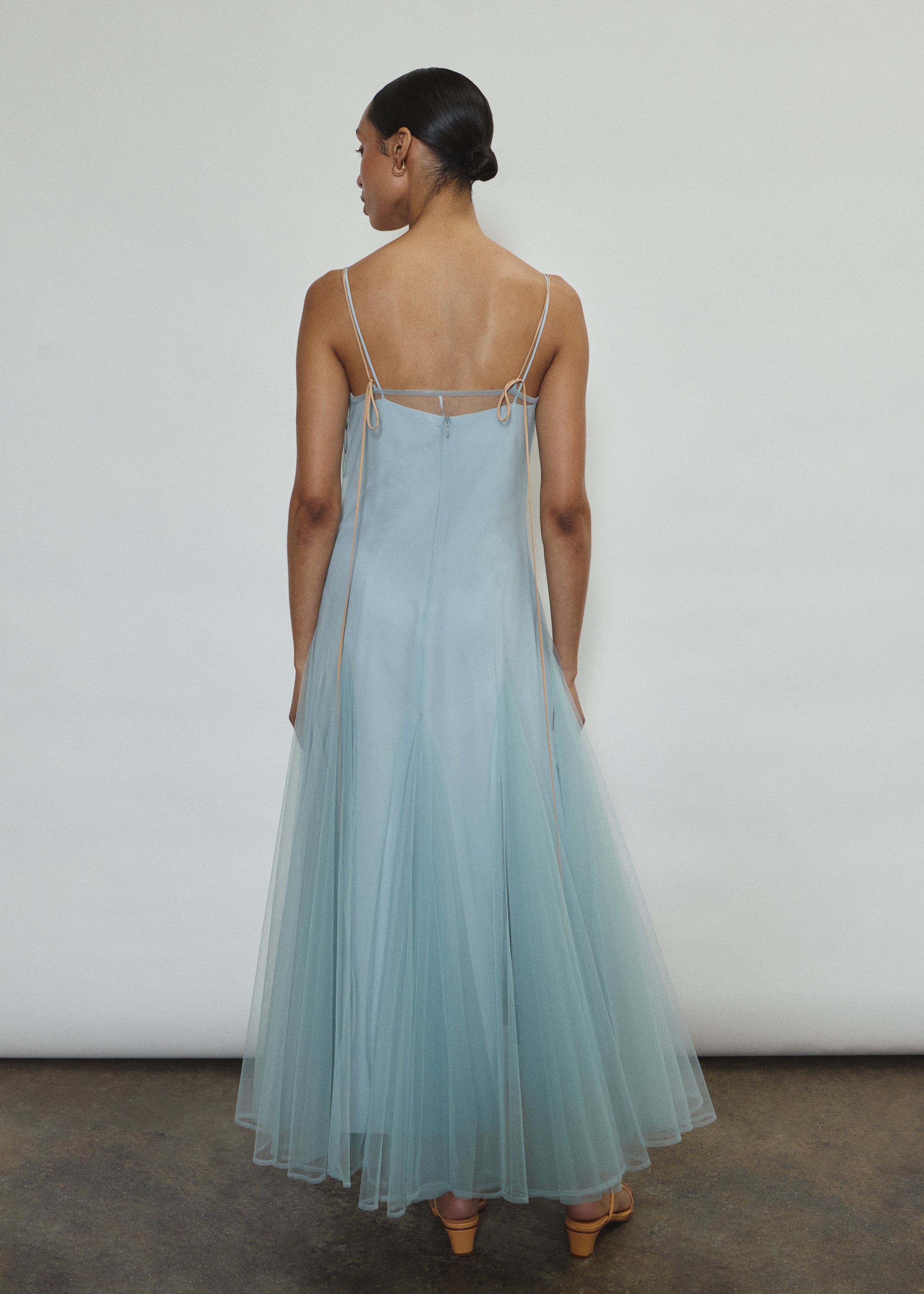Model wearing the blue Kamperett Camille Dress, a sheer tulle tea-length overlay featuring adjustable silk corded straps and a voluminous godet-pleated skirt.