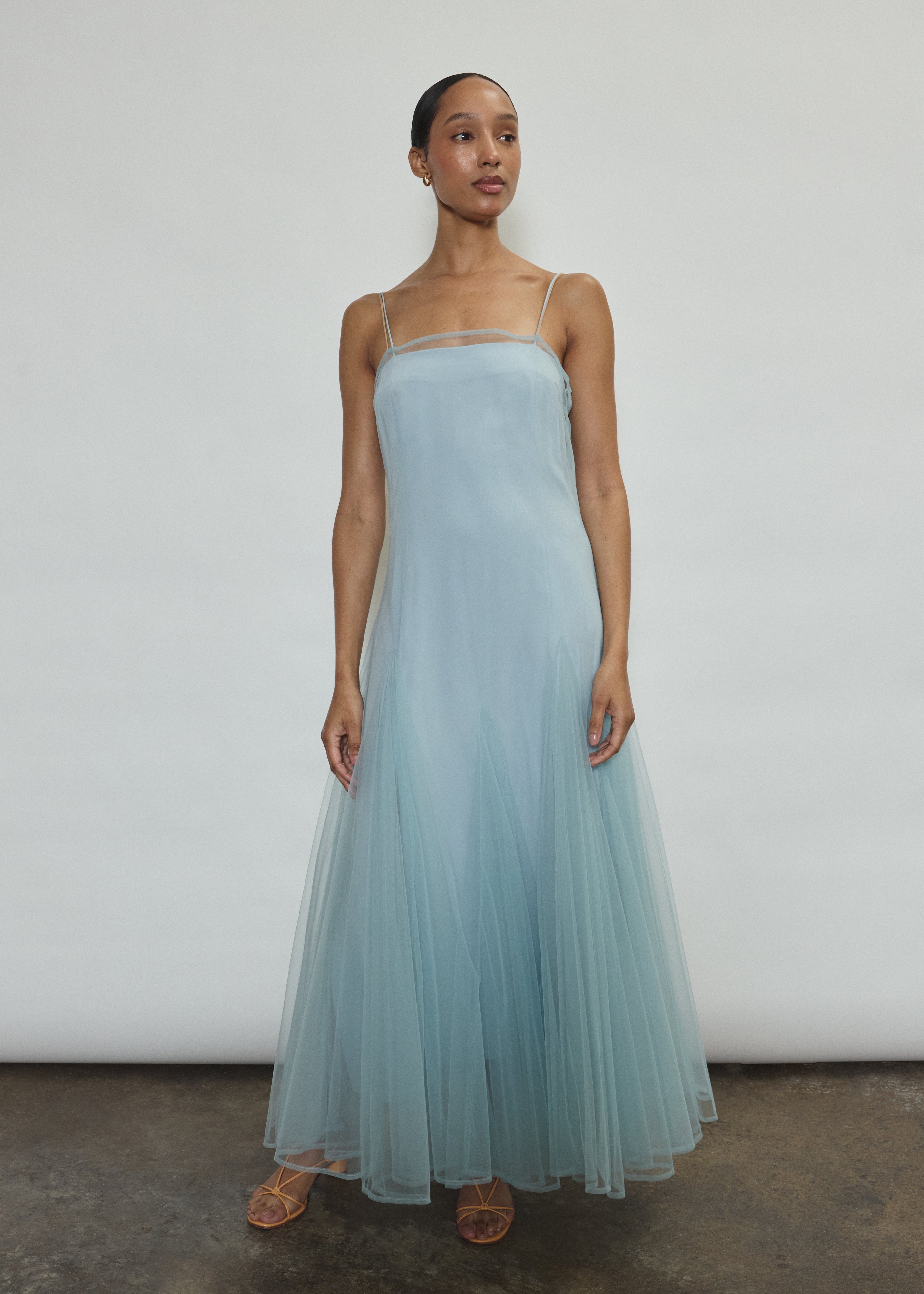 Model wearing the blue Kamperett Camille Dress, a sheer tulle tea-length overlay featuring adjustable silk corded straps and a voluminous godet-pleated skirt.