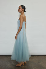 Model wearing the blue Kamperett Camille Dress, a sheer tulle tea-length overlay featuring adjustable silk corded straps and a voluminous godet-pleated skirt.