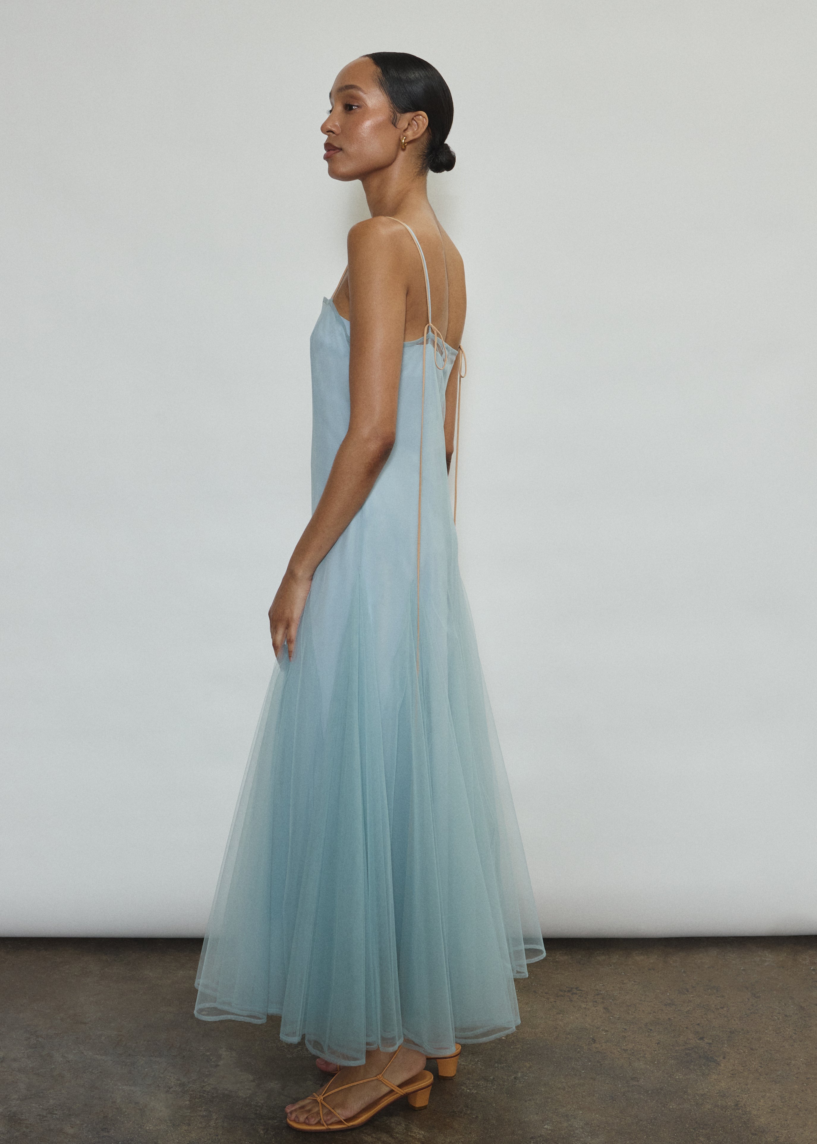 Model wearing the blue Kamperett Camille Dress, a sheer tulle tea-length overlay featuring adjustable silk corded straps and a voluminous godet-pleated skirt.