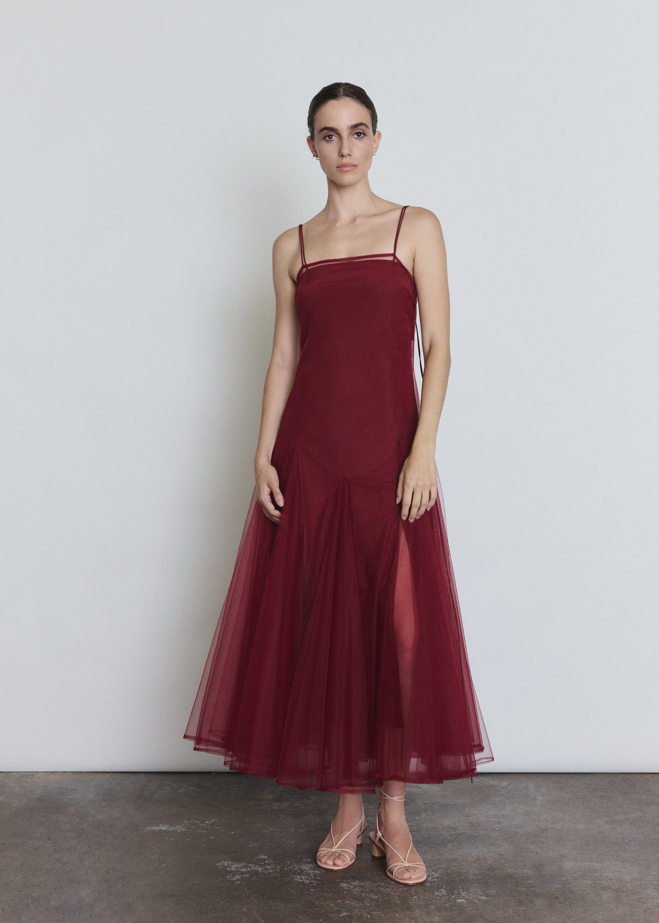 Front view of a model wearing the bordeaux sheer tulle Kamperett Camille Dress, a tea-length overlay with straight neckline and spaghetti straps.