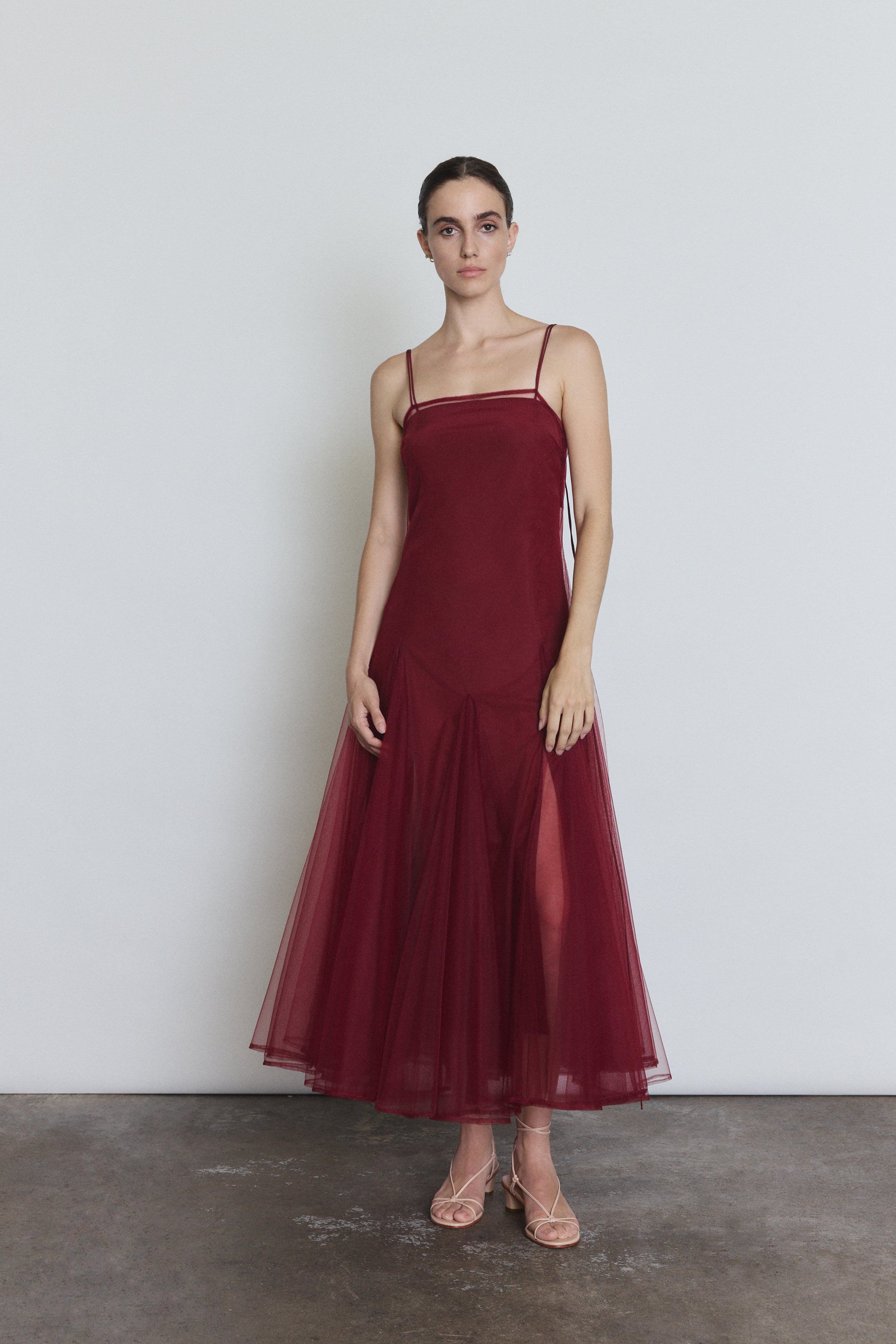 Front view of a model wearing the bordeaux sheer tulle Kamperett Camille Dress, a tea-length overlay with straight neckline and spaghetti straps.