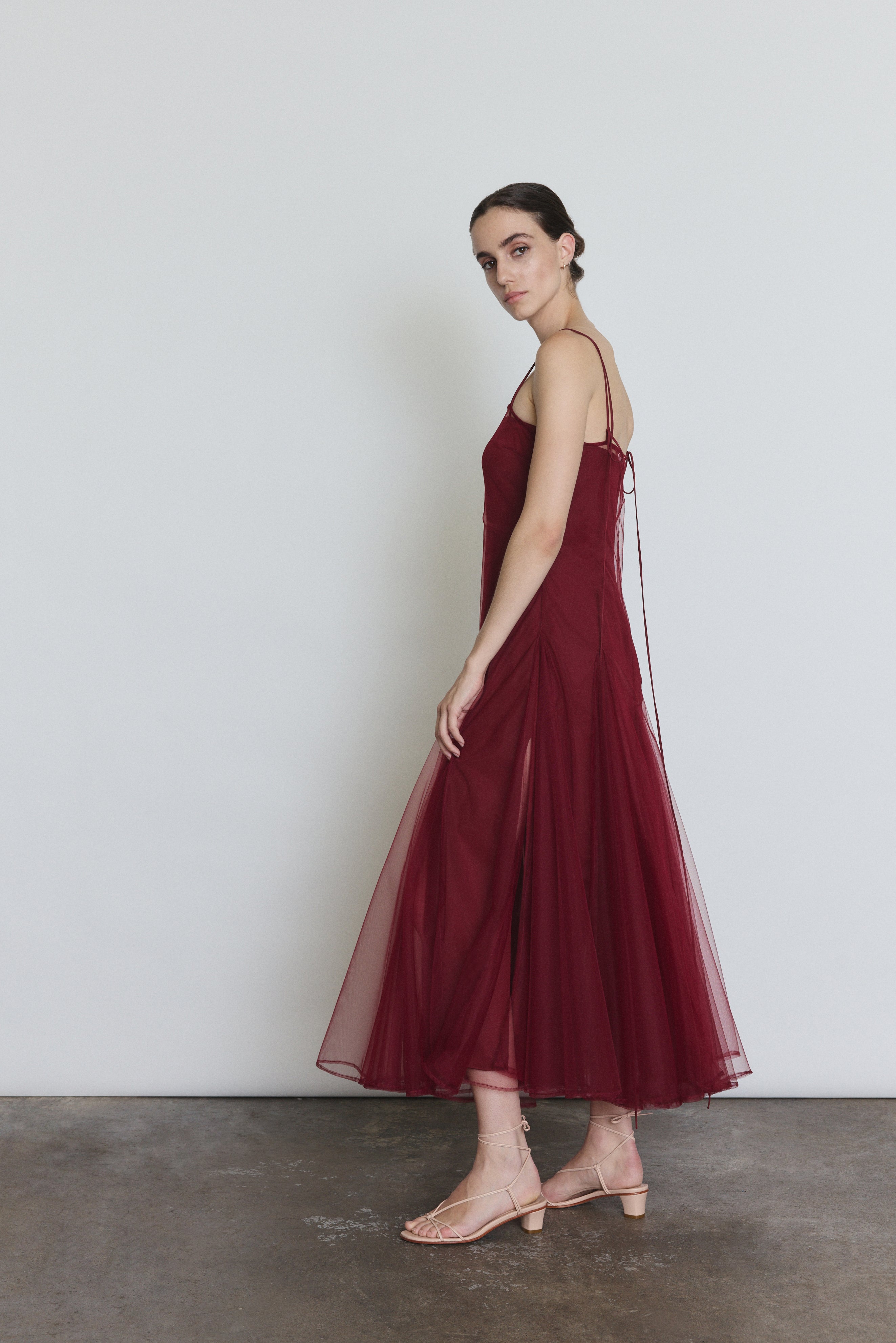 Side view of the bordeaux sheer tulle Kamperett Camille Dress showing the multi-godet full skirt.