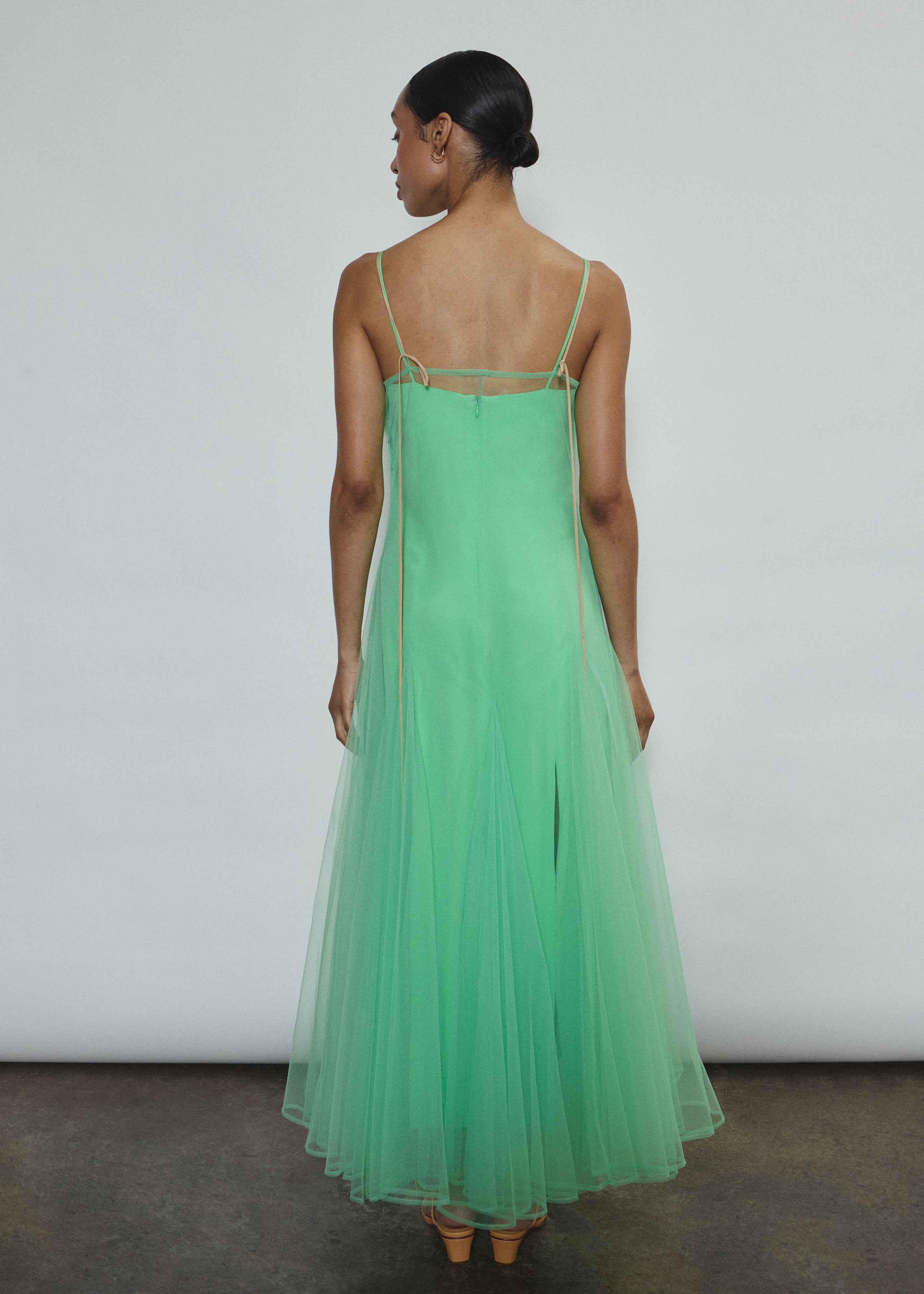 Model wearing the celadon Kamperett Camille Dress, a sheer tulle tea-length overlay featuring adjustable silk corded straps and a voluminous godet-pleated skirt.