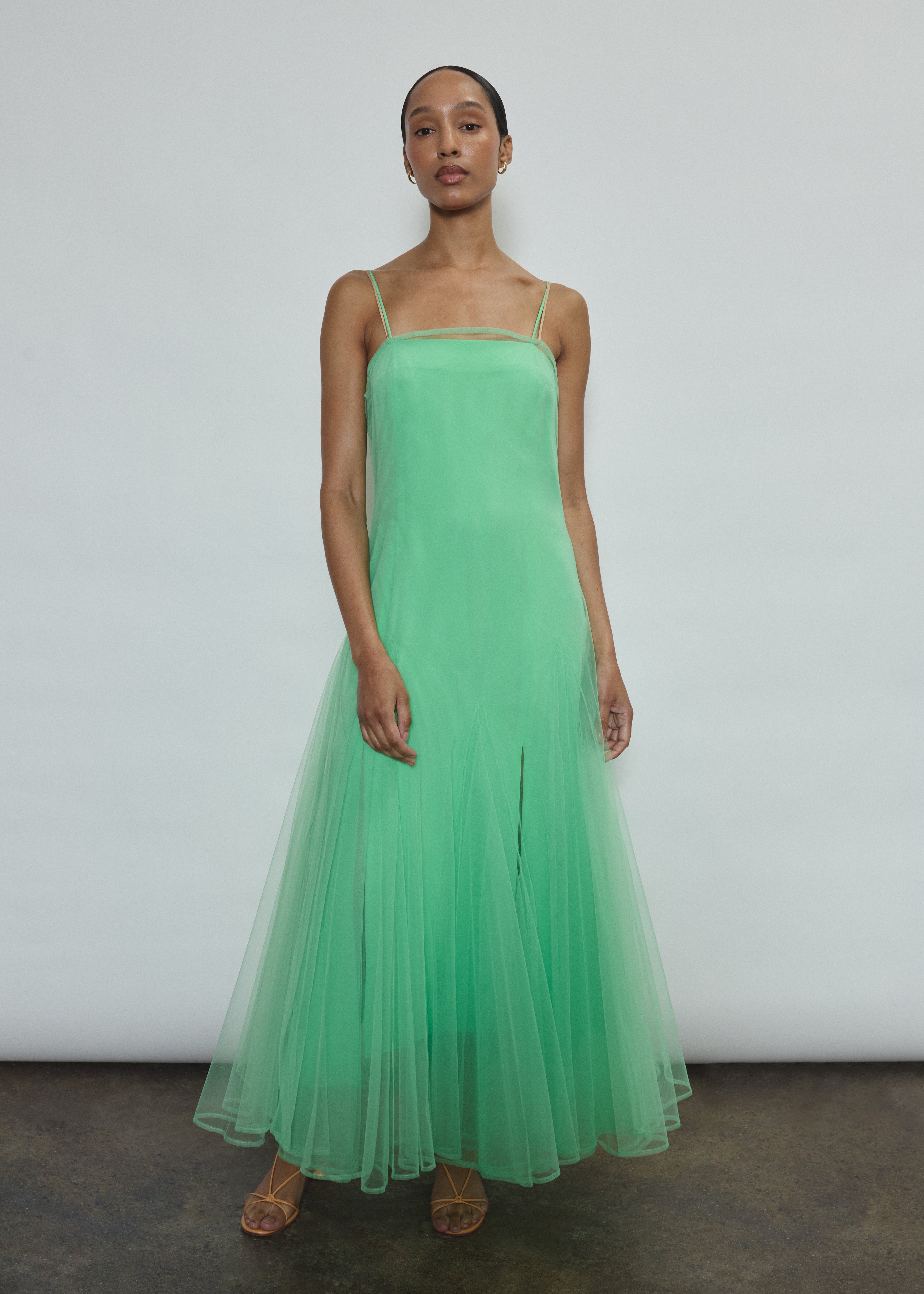 Model wearing the celadon Kamperett Camille Dress, a sheer tulle tea-length overlay featuring adjustable silk corded straps and a voluminous godet-pleated skirt.