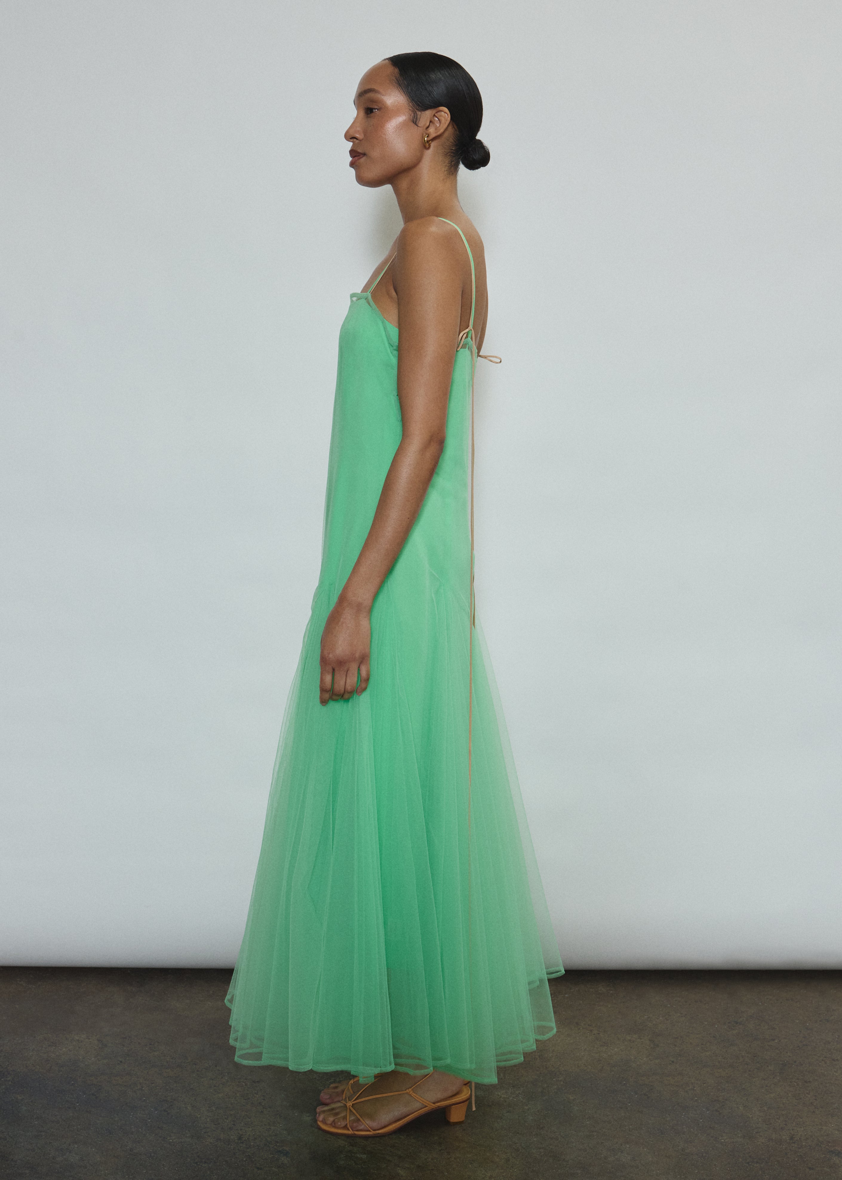 Model wearing the celadon Kamperett Camille Dress, a sheer tulle tea-length overlay featuring adjustable silk corded straps and a voluminous godet-pleated skirt.