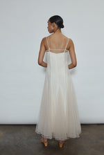 Model wearing the ivory Kamperett Camille Dress, a sheer tulle tea-length overlay featuring adjustable silk corded straps and a voluminous godet-pleated skirt.