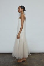 Model wearing the ivory Kamperett Camille Dress, a sheer tulle tea-length overlay featuring adjustable silk corded straps and a voluminous godet-pleated skirt.