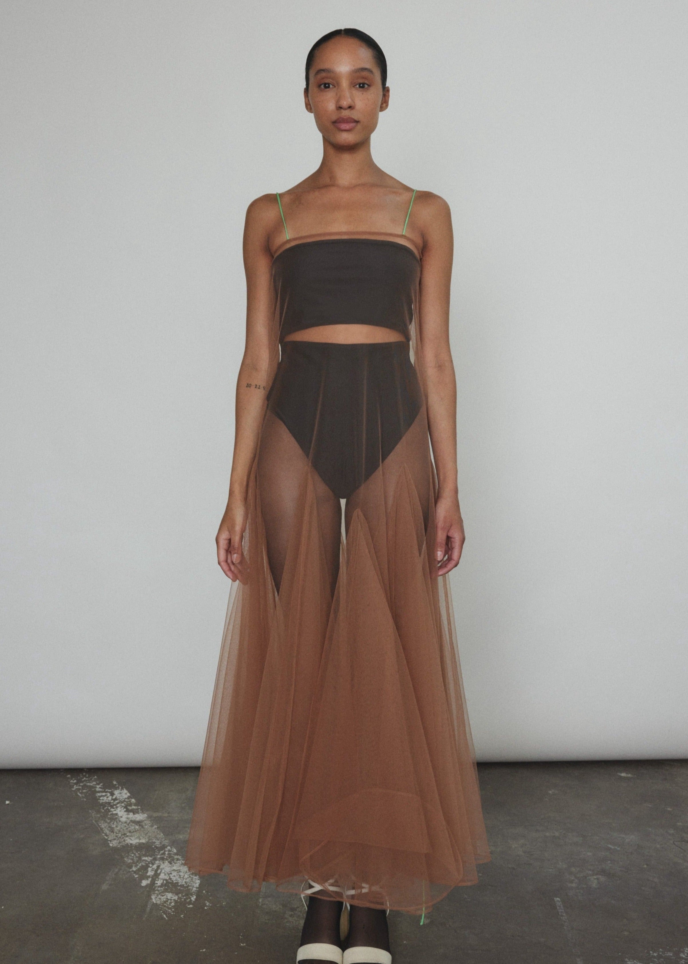 Model wearing the brown Kamperett Camille Dress, a sheer tulle tea-length overlay featuring adjustable silk corded straps and a voluminous godet-pleated skirt.
