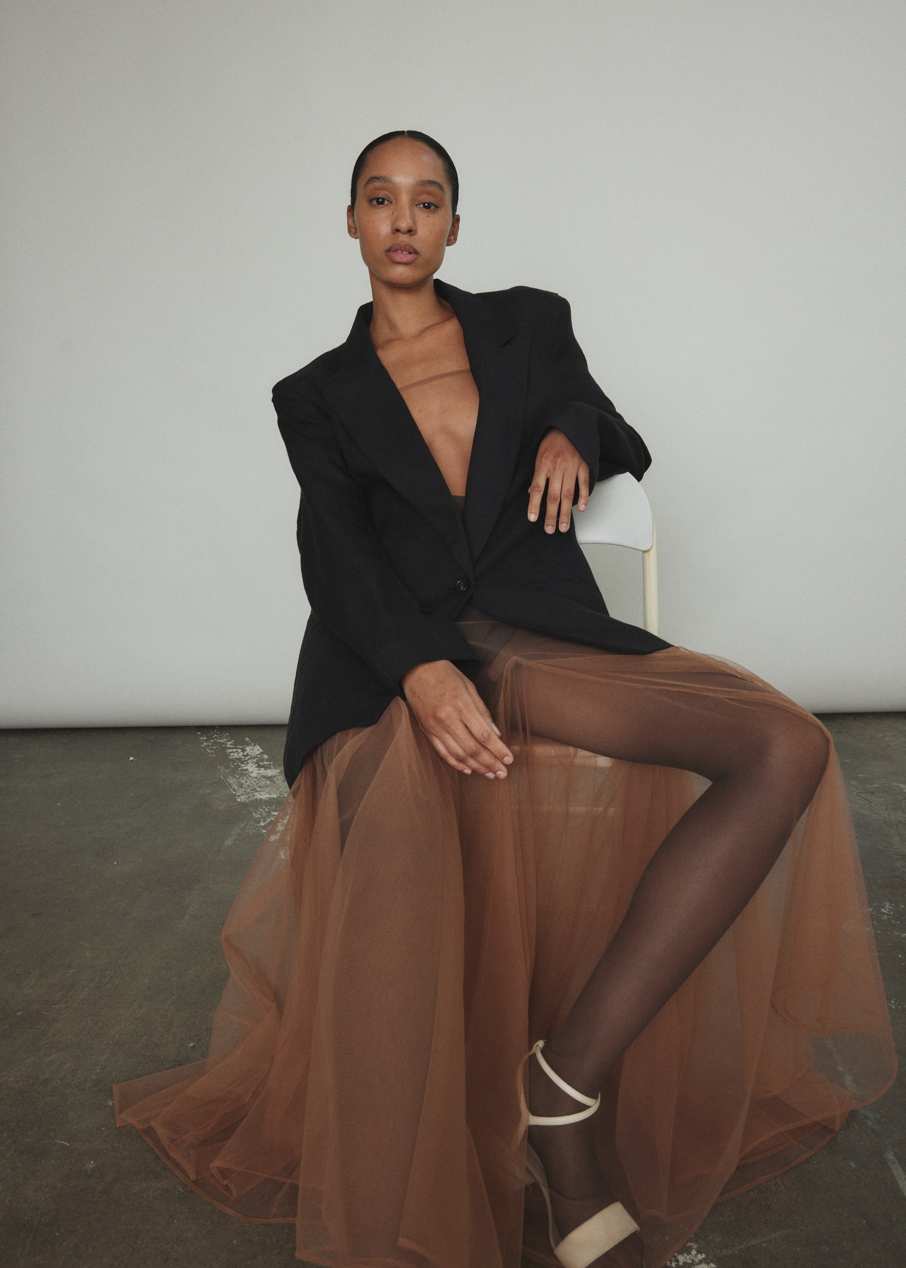 Model wearing the brown Kamperett Camille Dress, a sheer tulle tea-length overlay featuring adjustable silk corded straps and a voluminous godet-pleated skirt.