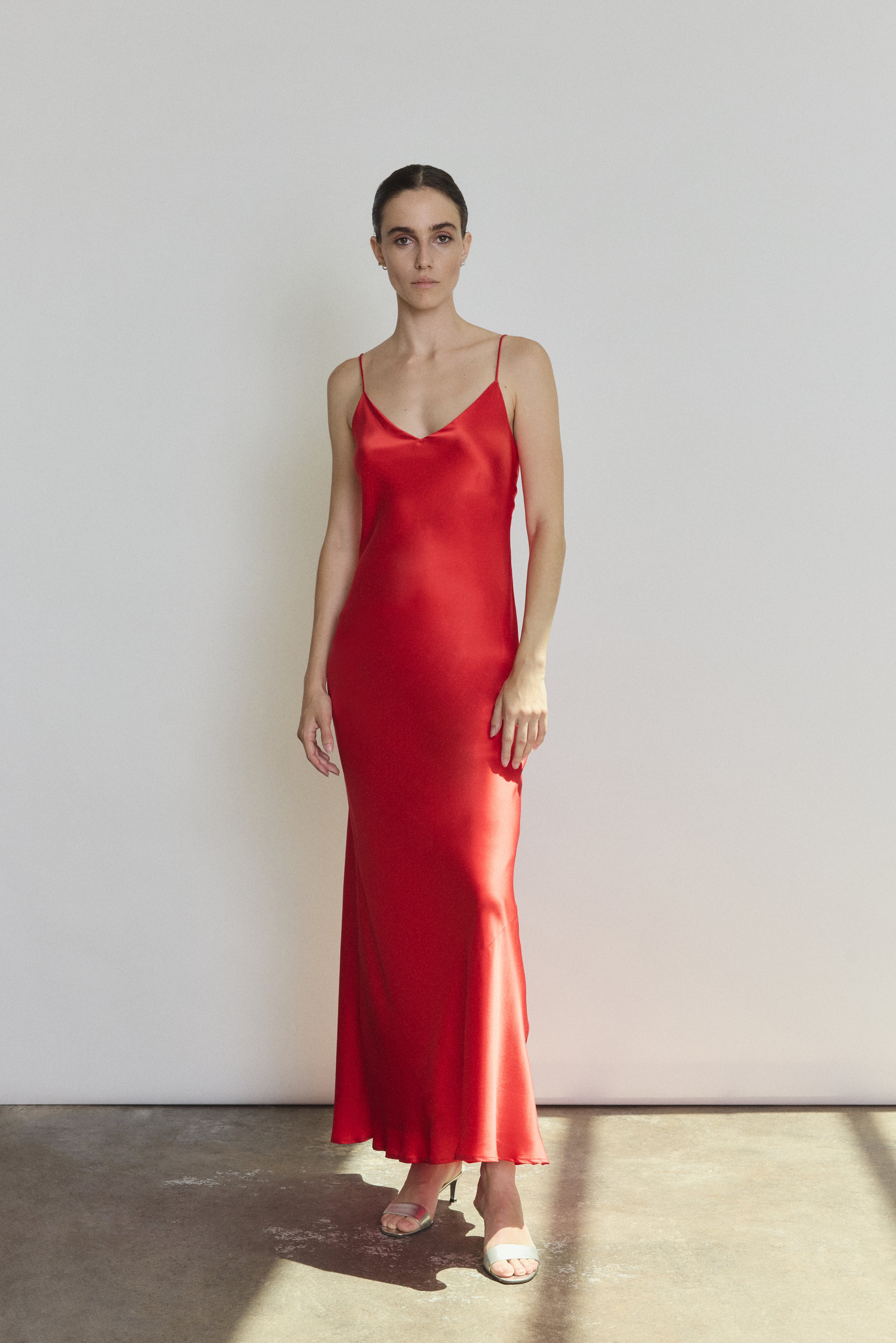 Front view of a model wearing the crimson silk charmeuse Kamperett Caroline Slip Dress, a bias-cut maxi slip with V neck and corded straps.