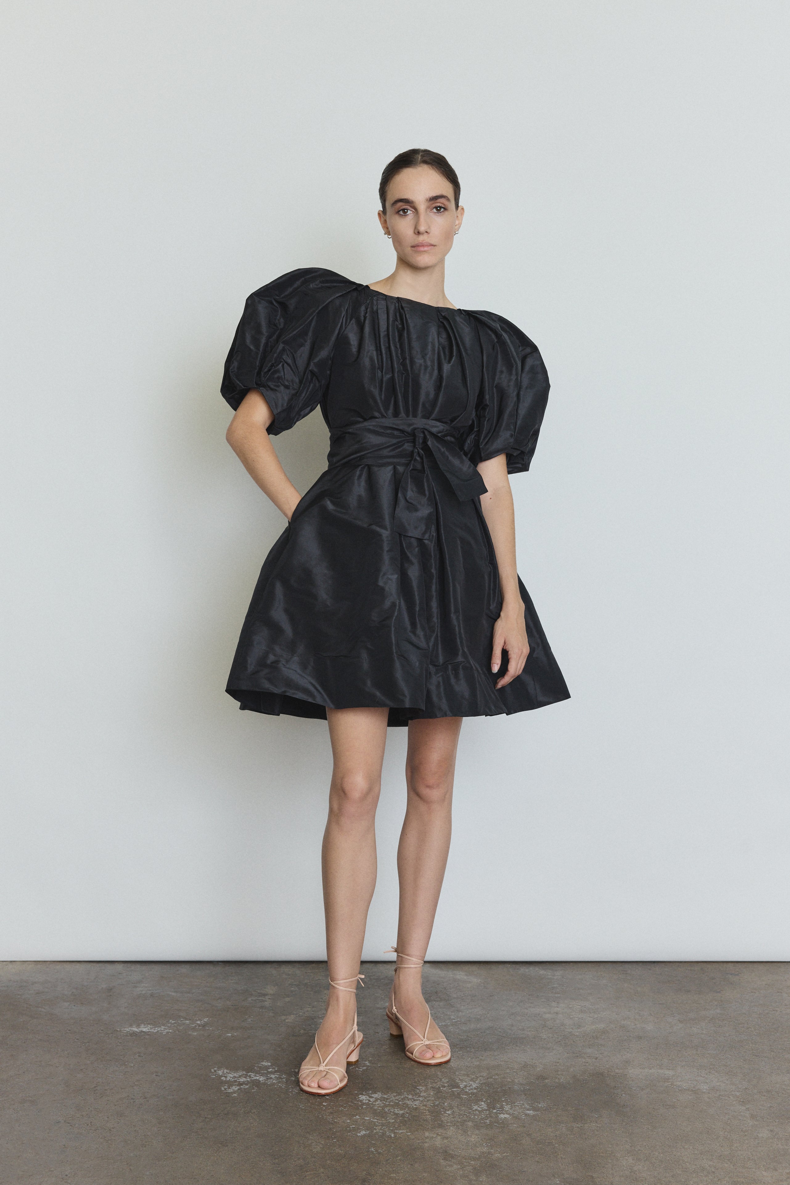 Editorial image of the black Kamperett Eva Dress cinched at the waist with the coordinating silk taffeta belt.