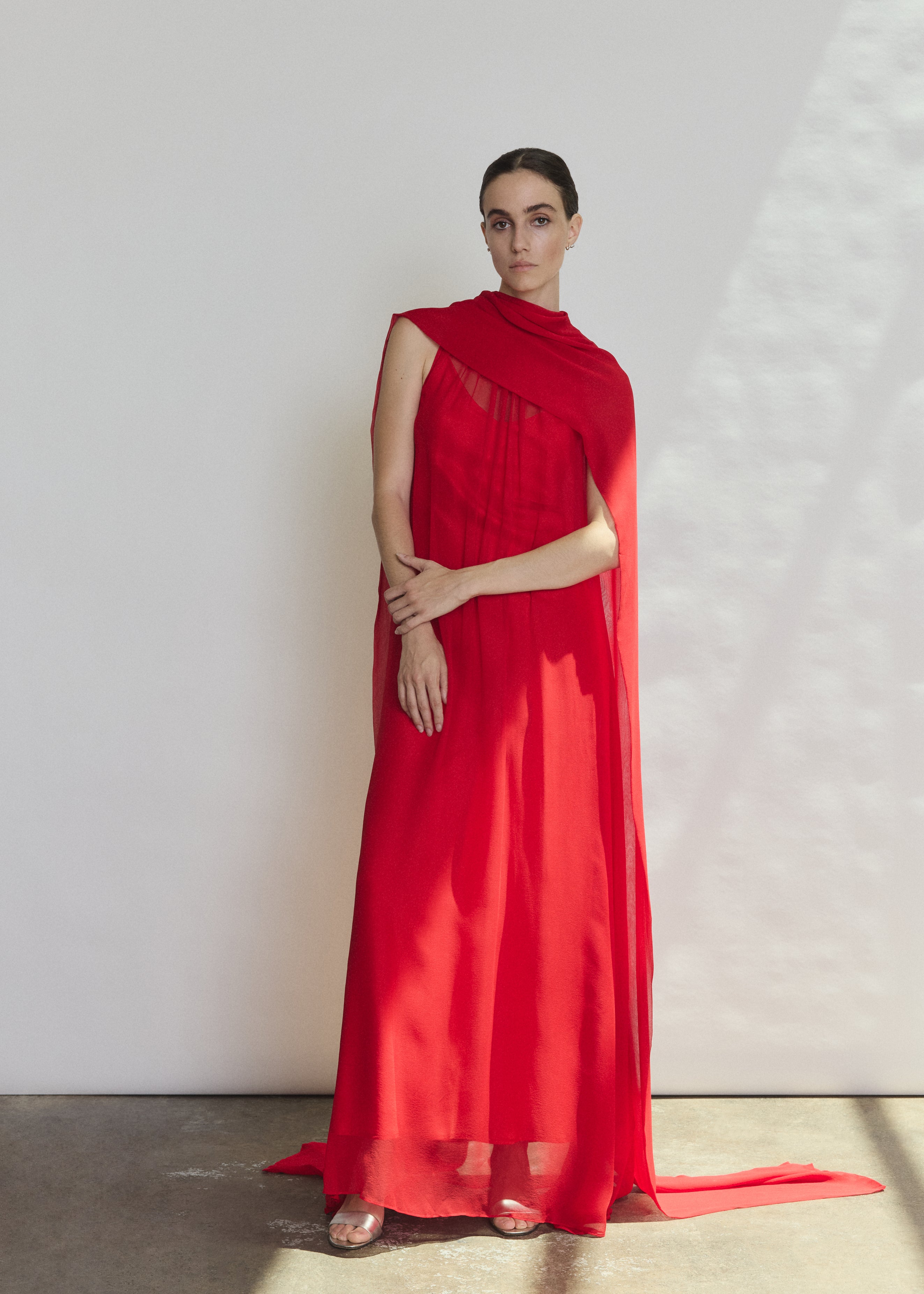 Front view of a model wearing the crimson silk chiffon Kamperett Iris Gown, a scarf-neck column gown with integrated capelet.