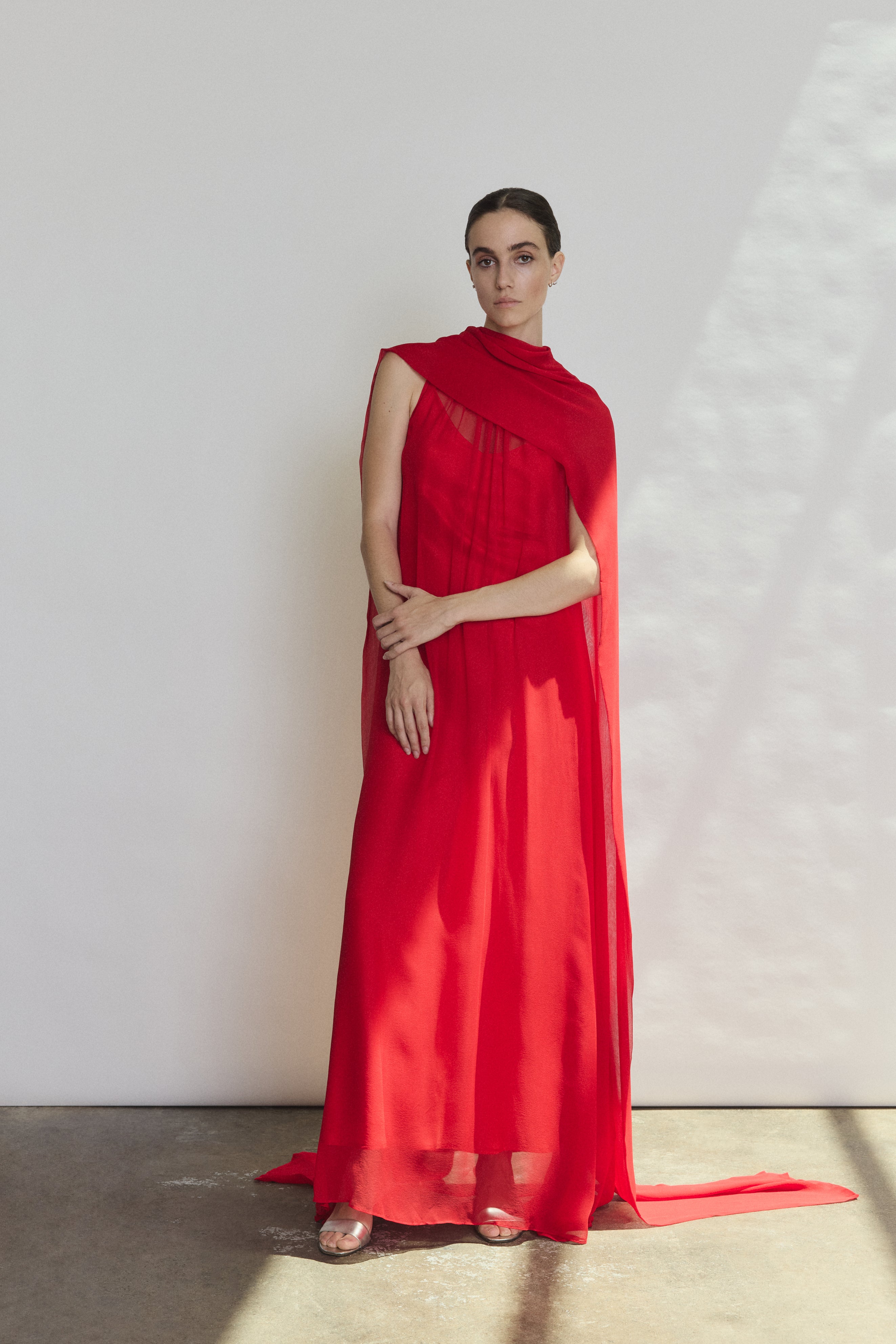 Front view of a model wearing the crimson silk chiffon Kamperett Iris Gown, a scarf-neck column gown with integrated capelet.