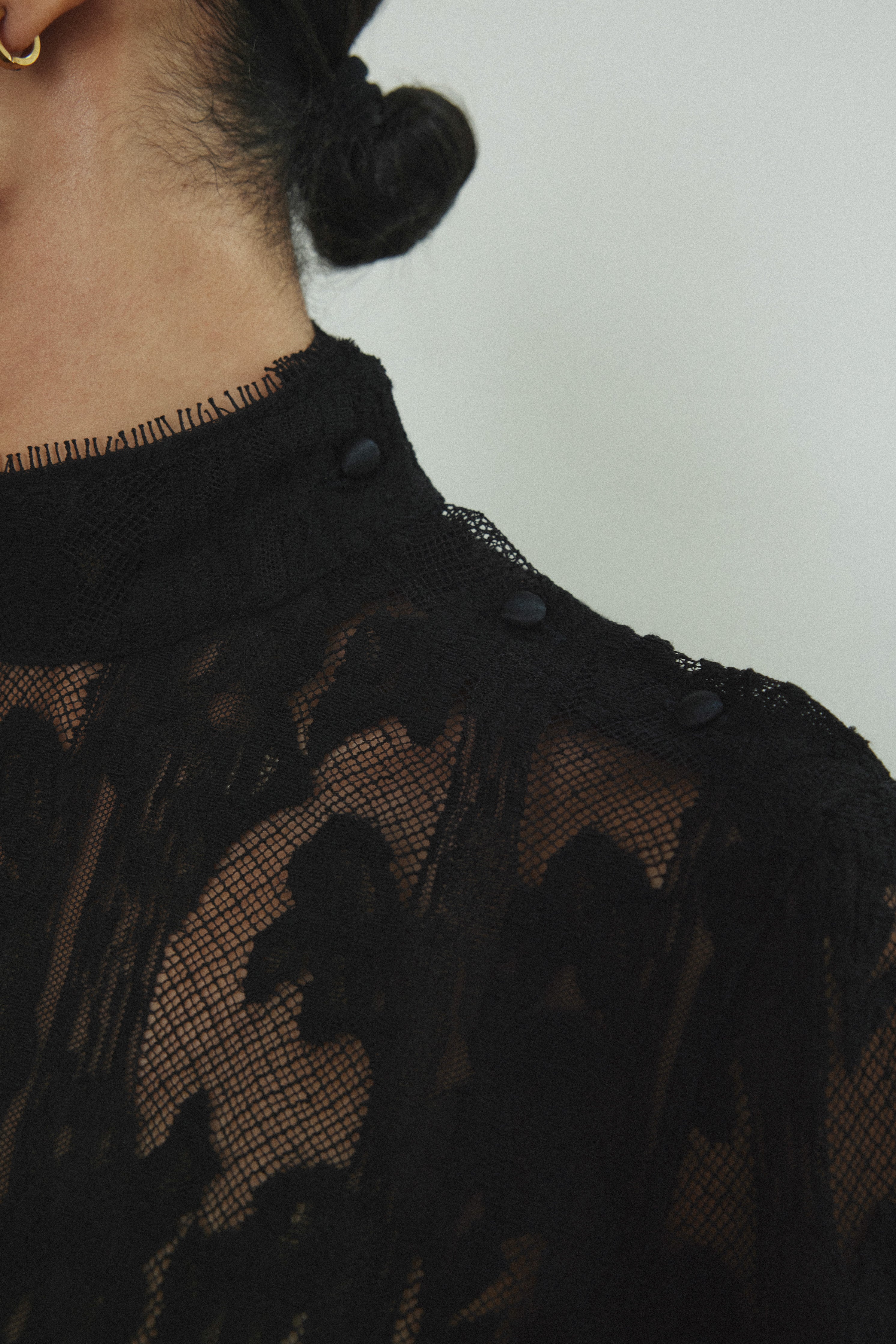 Kamperett Isabella Tunic in black French lace, editorial close-up of structured mock neck and button closure at shoulder seam.