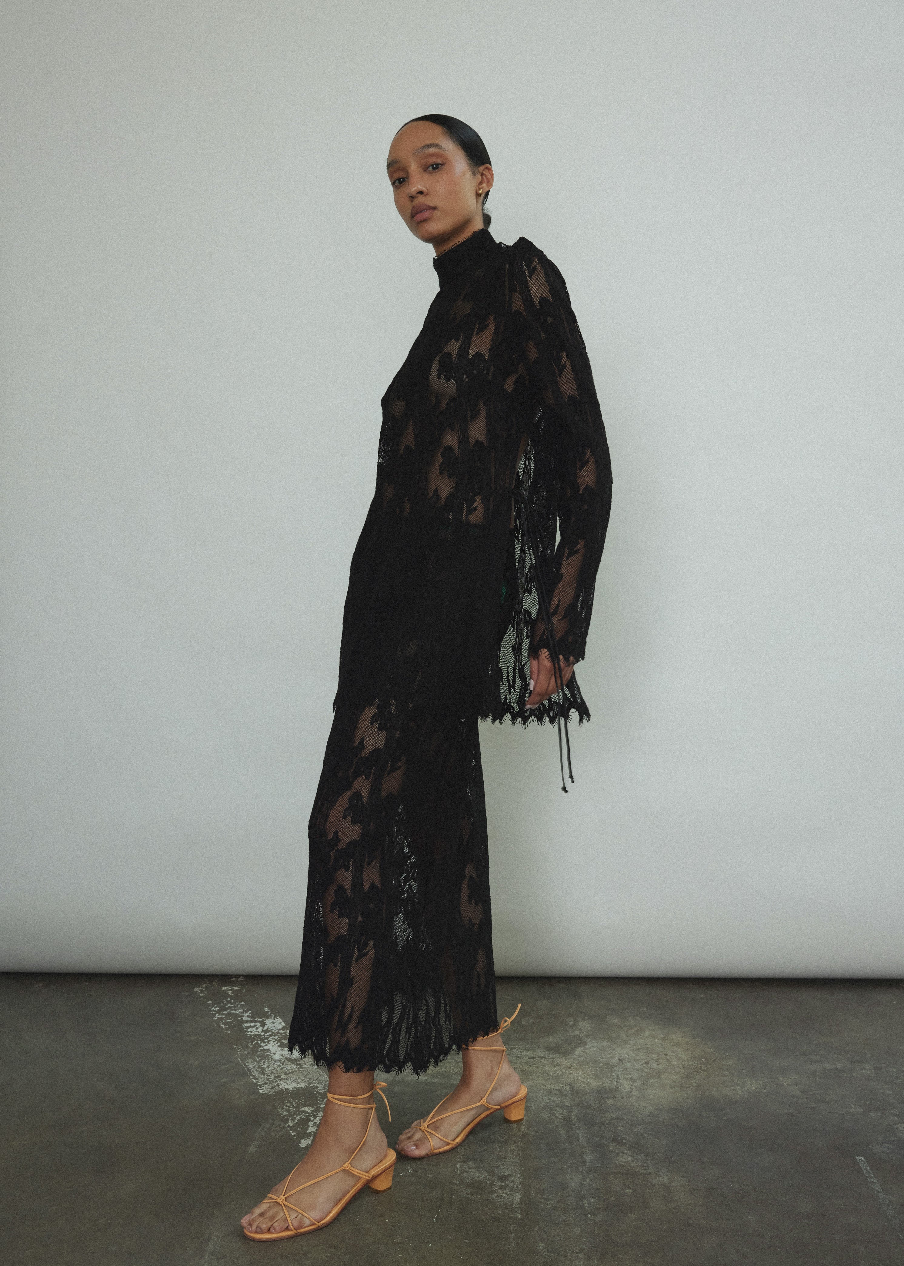 Kamperett Isabella Tunic in black French lace, full-length side view showing straight-cut silhouette, mock neck, eyelash lace hem, and long sleeves with wrist zipper closure.