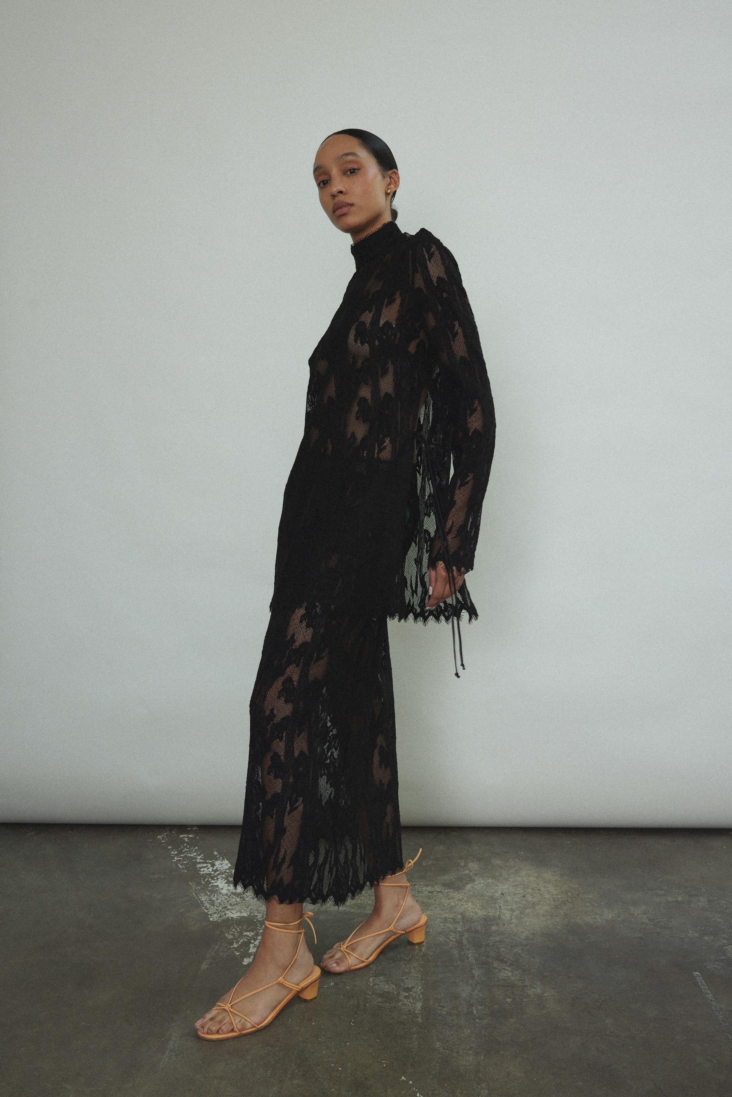 Kamperett Isabella Tunic in black French lace, full-length side view showing straight-cut silhouette, mock neck, eyelash lace hem, and long sleeves with wrist zipper closure.