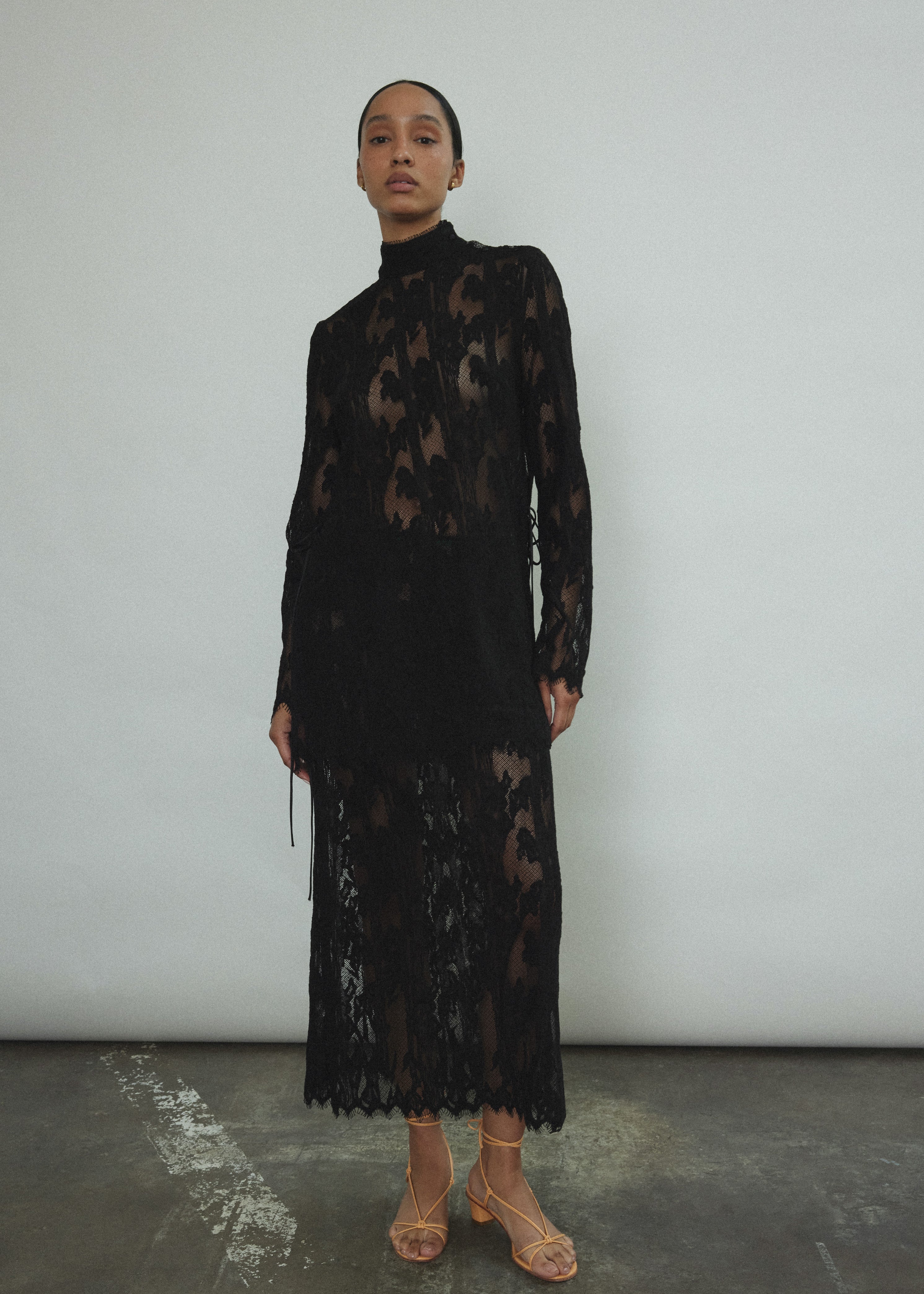 Kamperett Isabella Tunic in black French lace, full-length front view showing straight-cut silhouette, mock neck, eyelash lace hem, and long sleeves with wrist zipper closure.