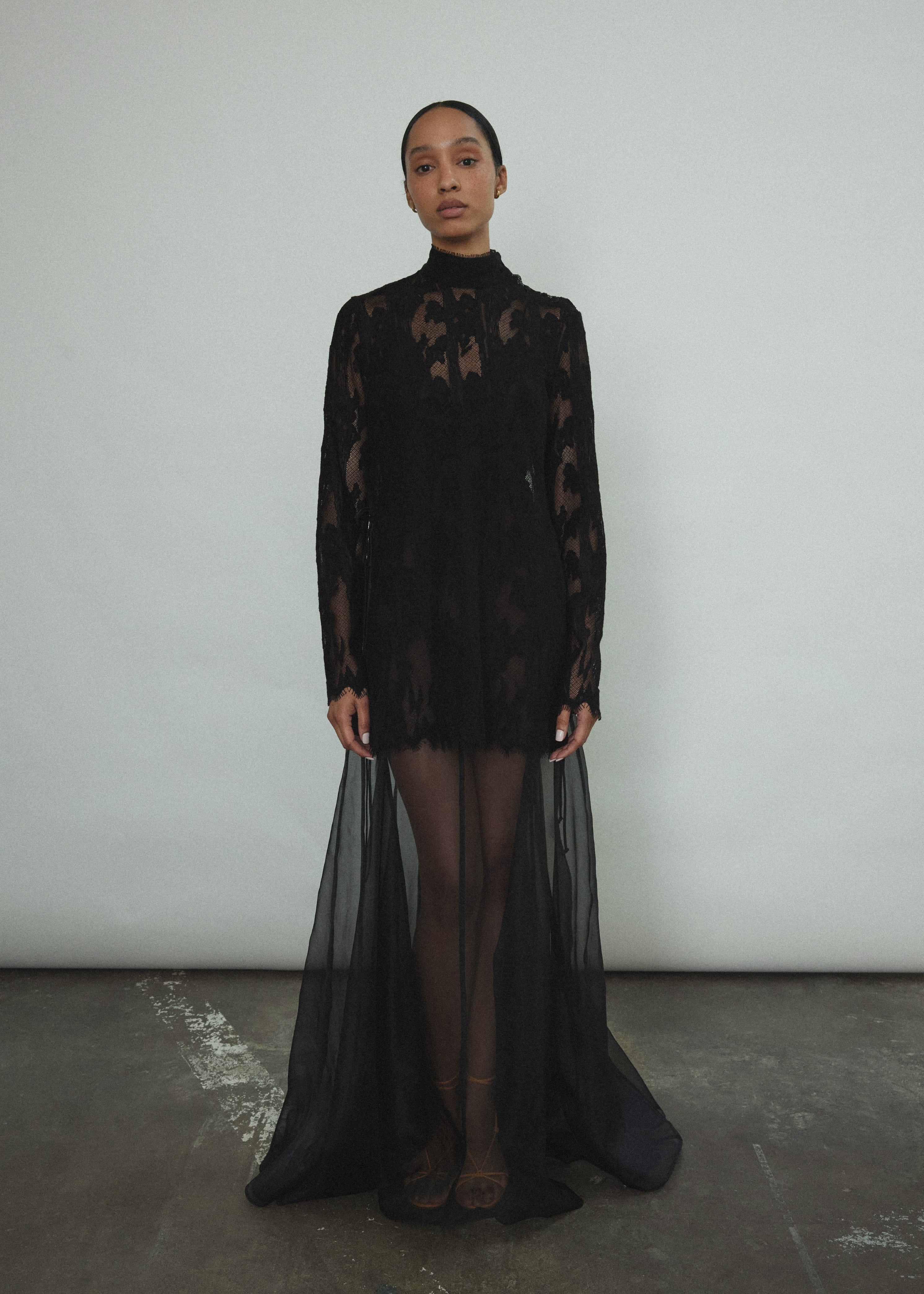 Kamperett Isabella Tunic in black French lace, full-length front view showing straight-cut silhouette, mock neck, eyelash lace hem, and long sleeves with wrist zipper closure.