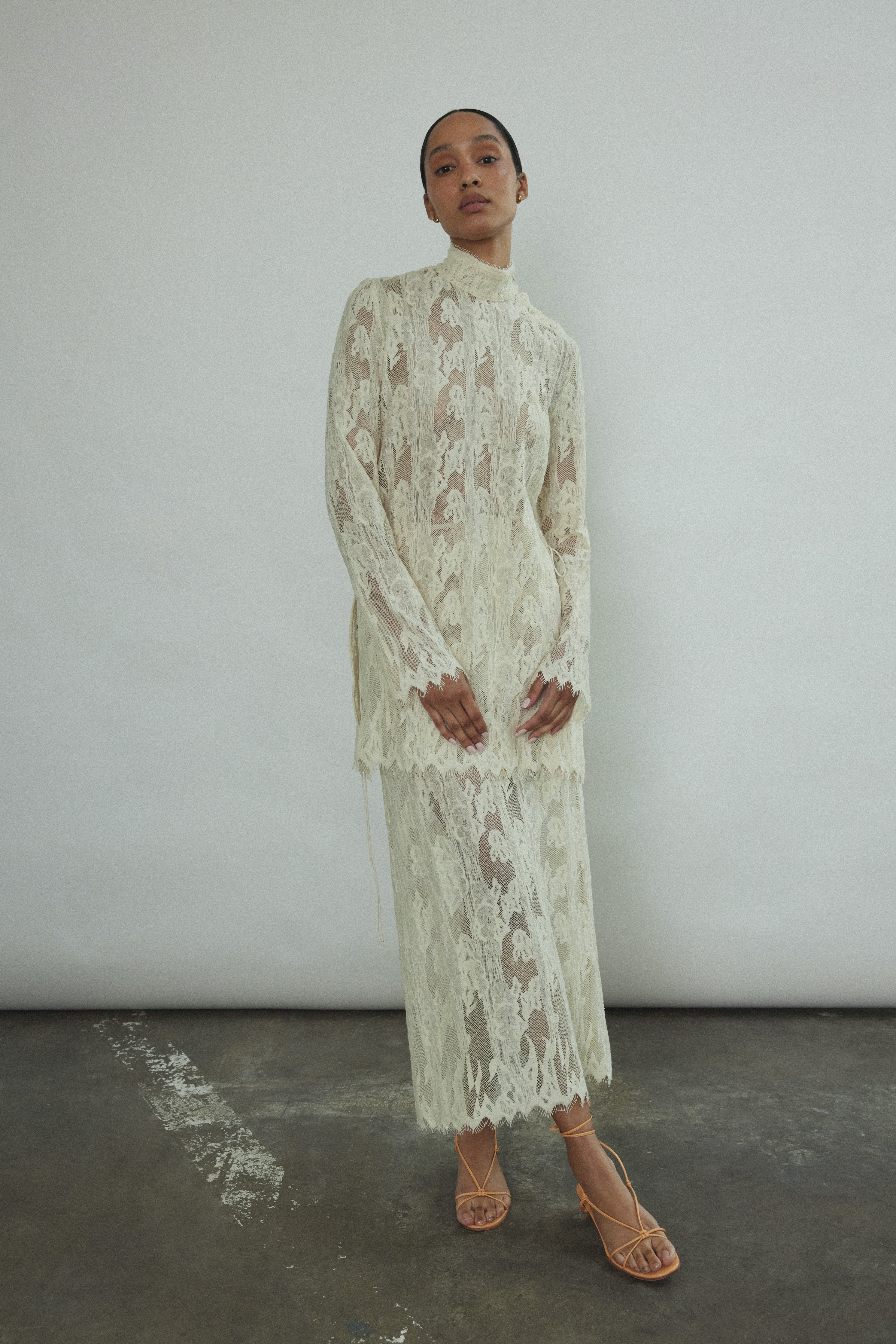 Kamperett Isabella Tunic in cream French lace, full-length front view showing straight-cut silhouette, mock neck, eyelash lace hem, and long sleeves with wrist zipper closure.